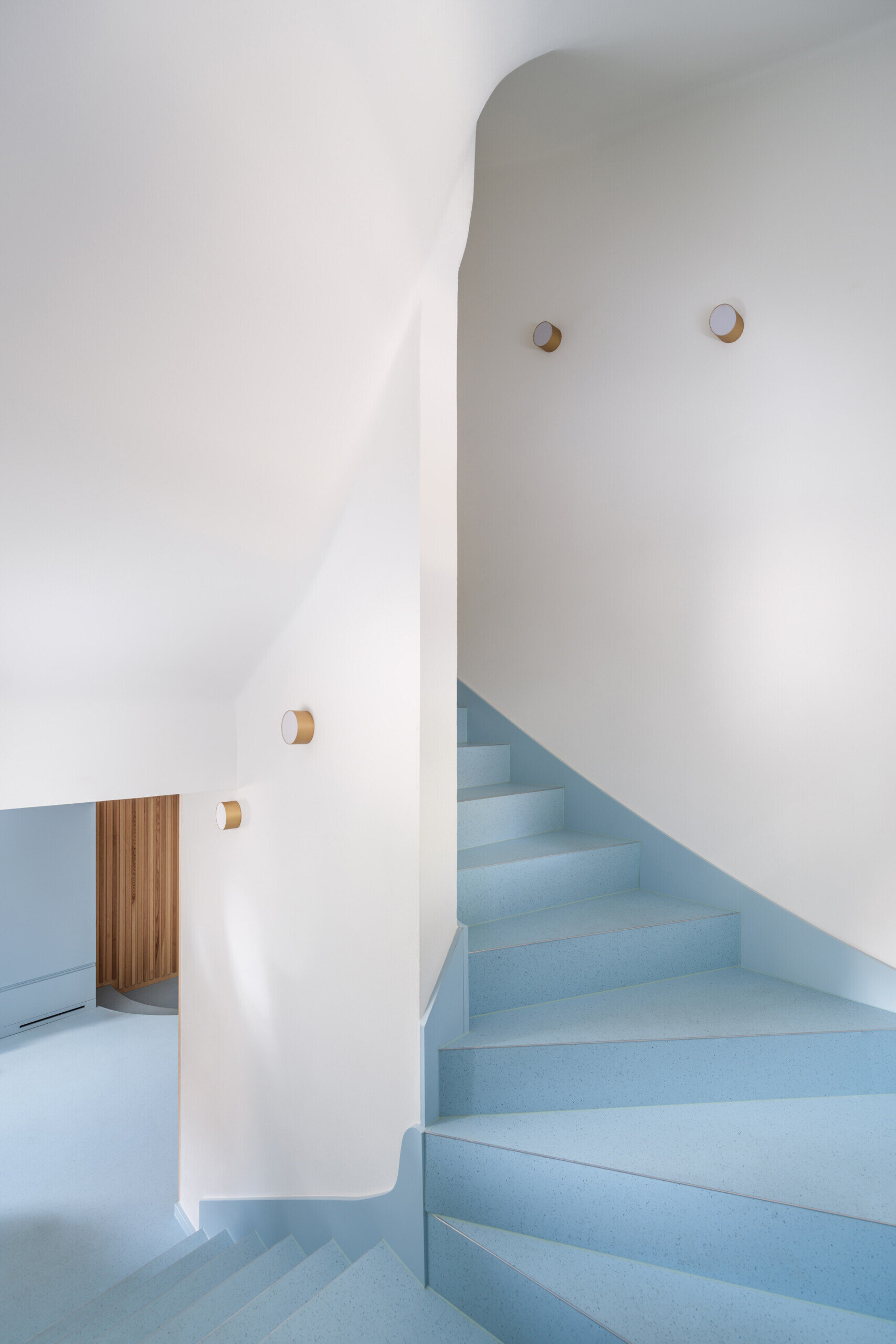 Discover the colorful architectural details inside this modernist house renovation in Prague. A curved staircase with pale blue steps, slender red railings, and subtle red accents along doors, baseboards, and furniture introduces an unexpected design element.