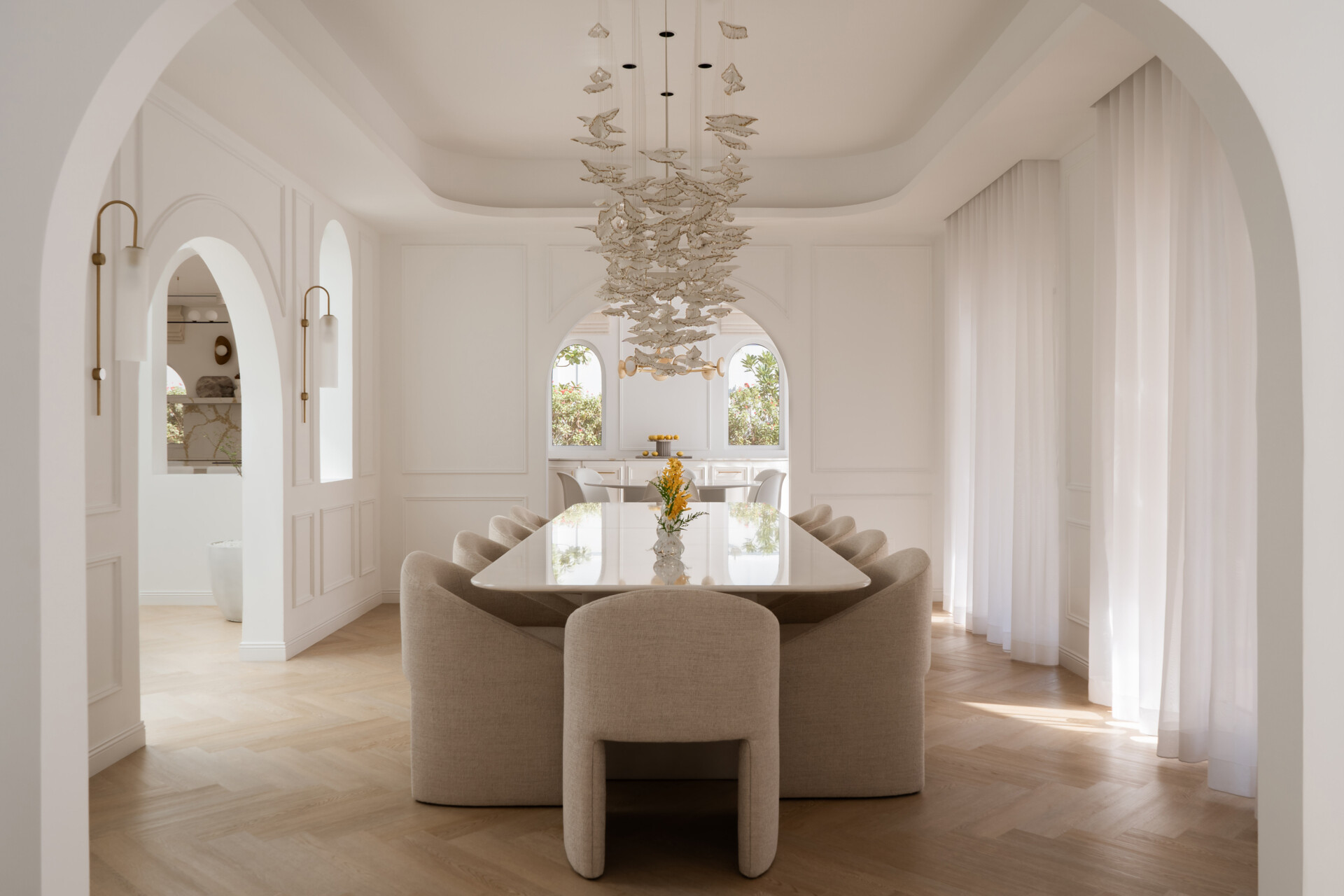 This luxurious formal dining room in Dubai features a monumental white onyx dining table by DOT Objects, sculptural arched bases, curved upholstered dining chairs, and an incredible suspended leaf installation. Designed by D’Ora Tokai Designs for The White Arcade.