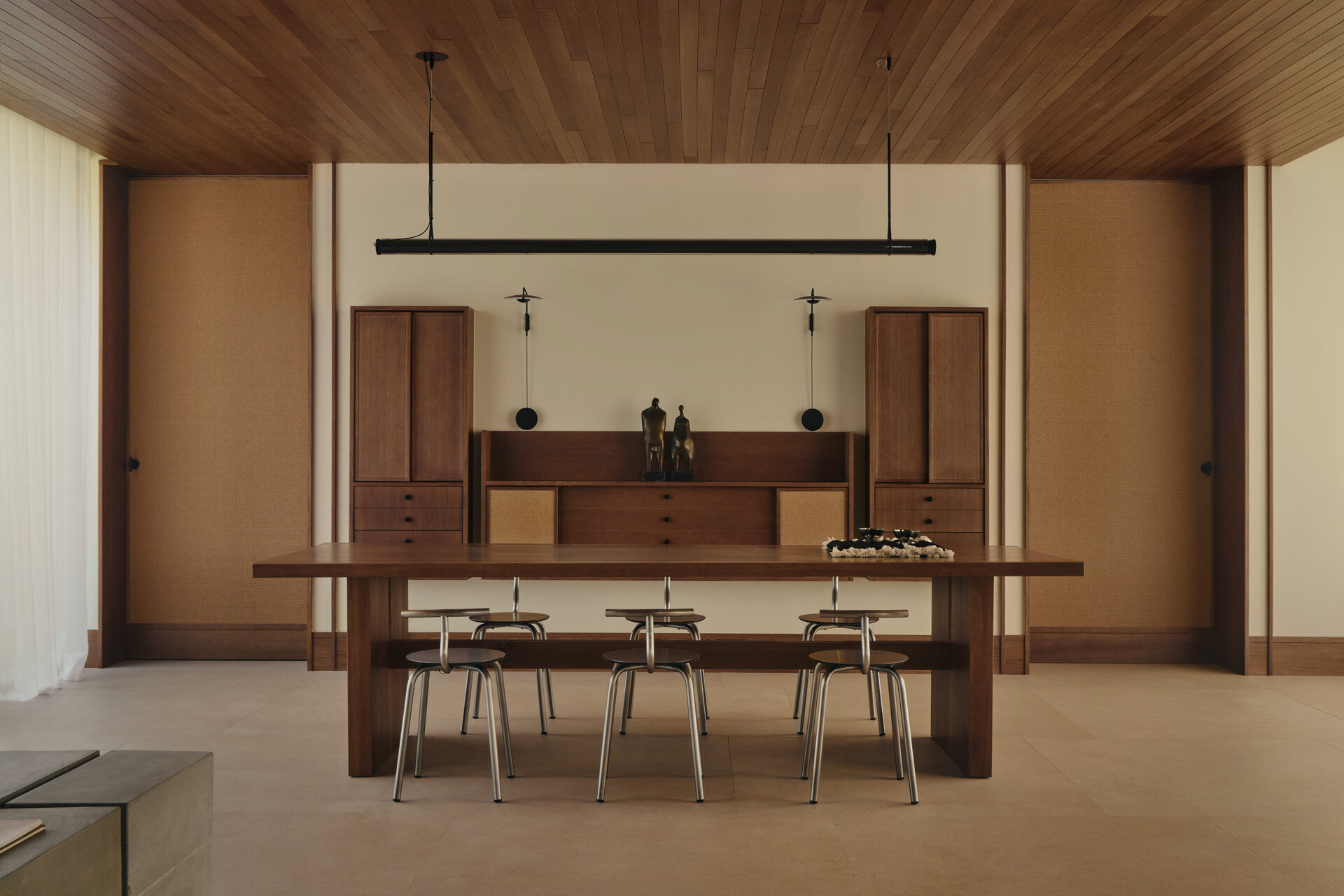 This contemporary dining room by Viruta Lab features a custom walnut dining table, metal-framed chairs, natural woven cabinetry, minimalist lighting, and sculptural decor.