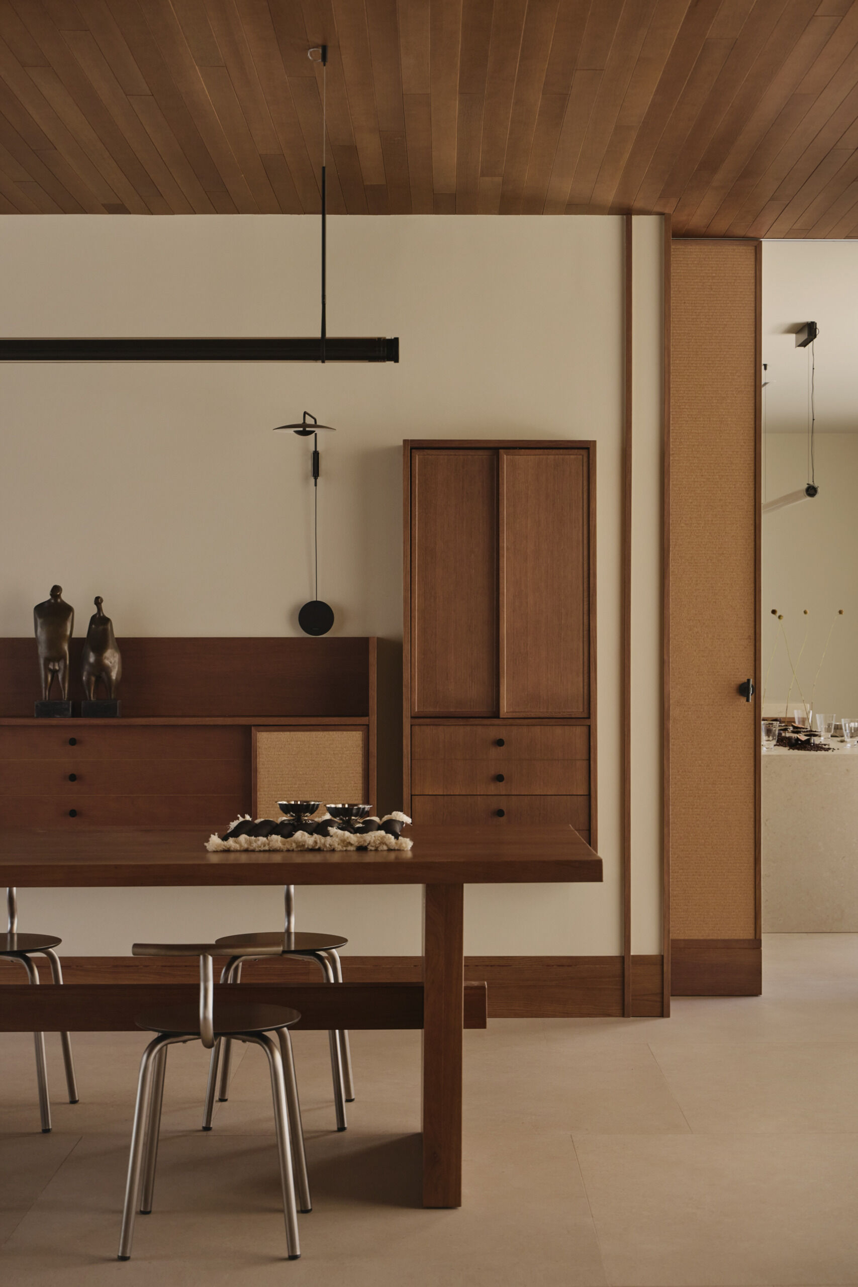 This contemporary dining room by Viruta Lab features a custom walnut dining table, metal-framed chairs, natural woven cabinetry, minimalist lighting, and sculptural decor.