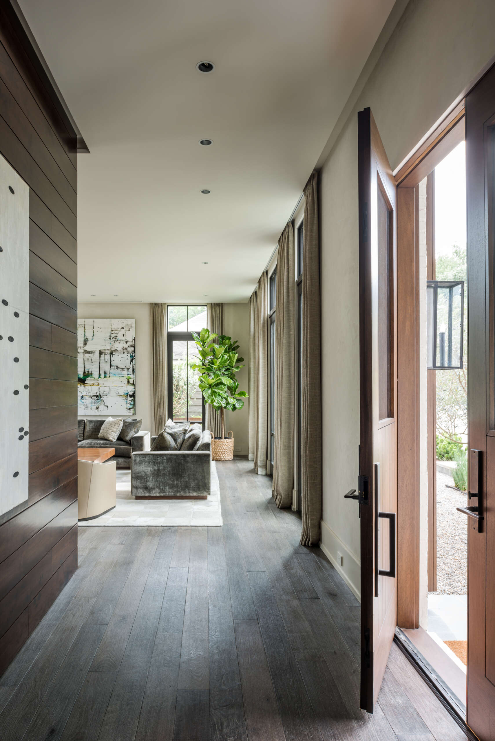 A contemporary front entryway with double wood doors, dark wood floors, horizontal wall paneling, recessed lighting, and a direct view into the living room.