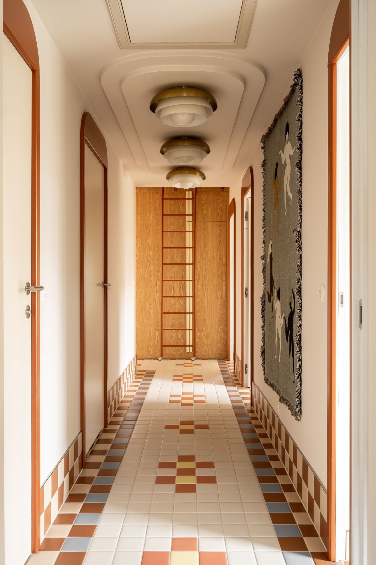 Colorful hallway design with floral-inspired mosaic floor tiles, terracotta arched doorframes, decorative ceiling lights, custom wood storage, and playful multicolored pendant lighting.