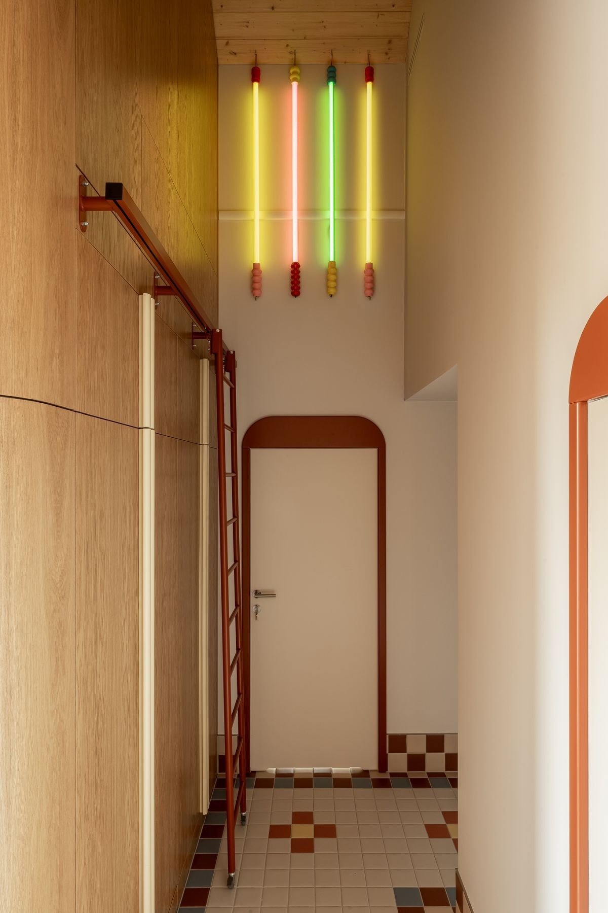 Colorful hallway design with floral-inspired mosaic floor tiles, terracotta arched doorframes, decorative ceiling lights, custom wood storage, and playful multicolored pendant lighting.