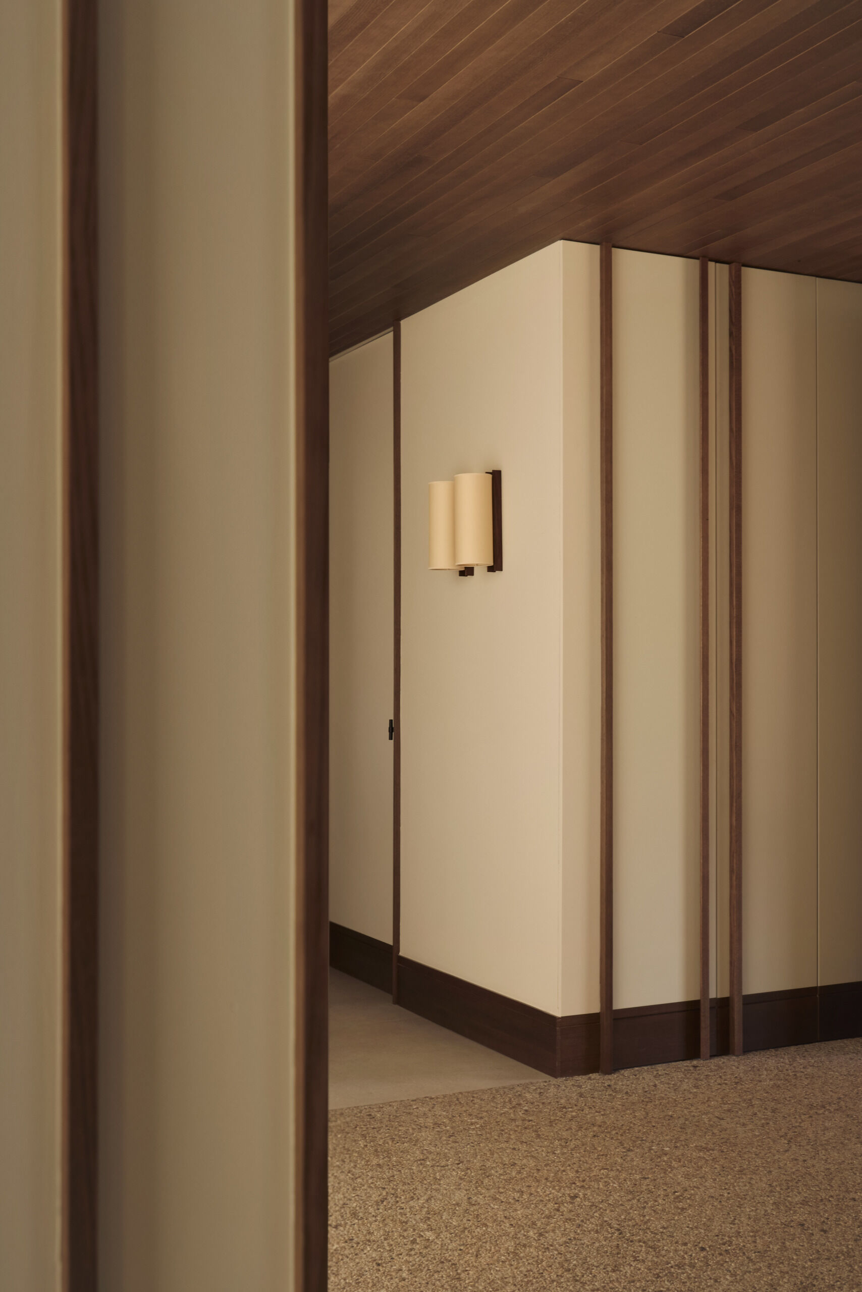 This modern hallway in Spain features natural woven wall panels, concealed doors, warm timber ceilings, sheer curtains, and courtyard windows that bring in natural light.