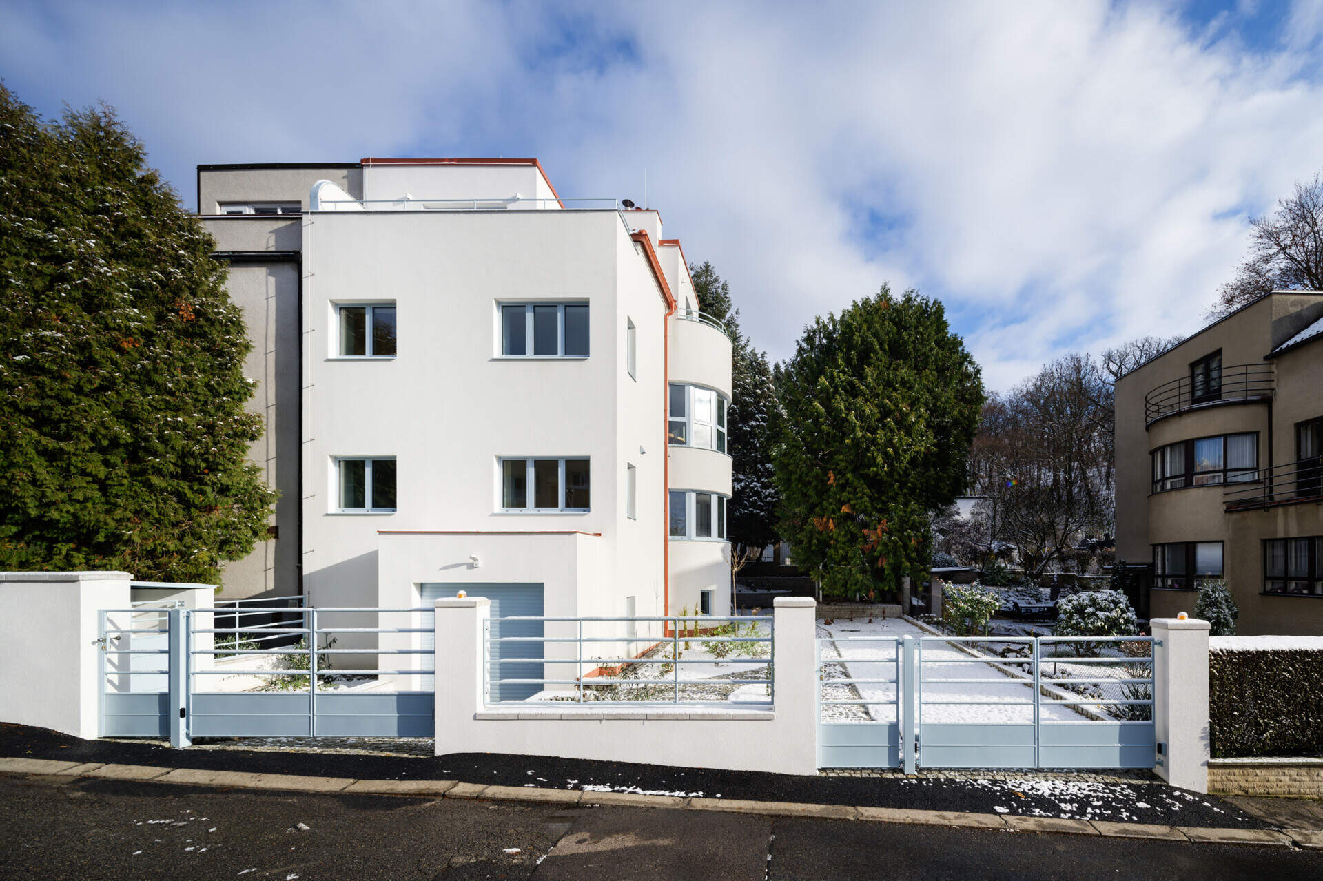Discover the exterior transformation of Blue Window House in Prague, Czech Republic, by No Architects. The renovated modernist home features a white facade, curved window bays, distinctive blue aluminum window frames, and a redesigned garden.