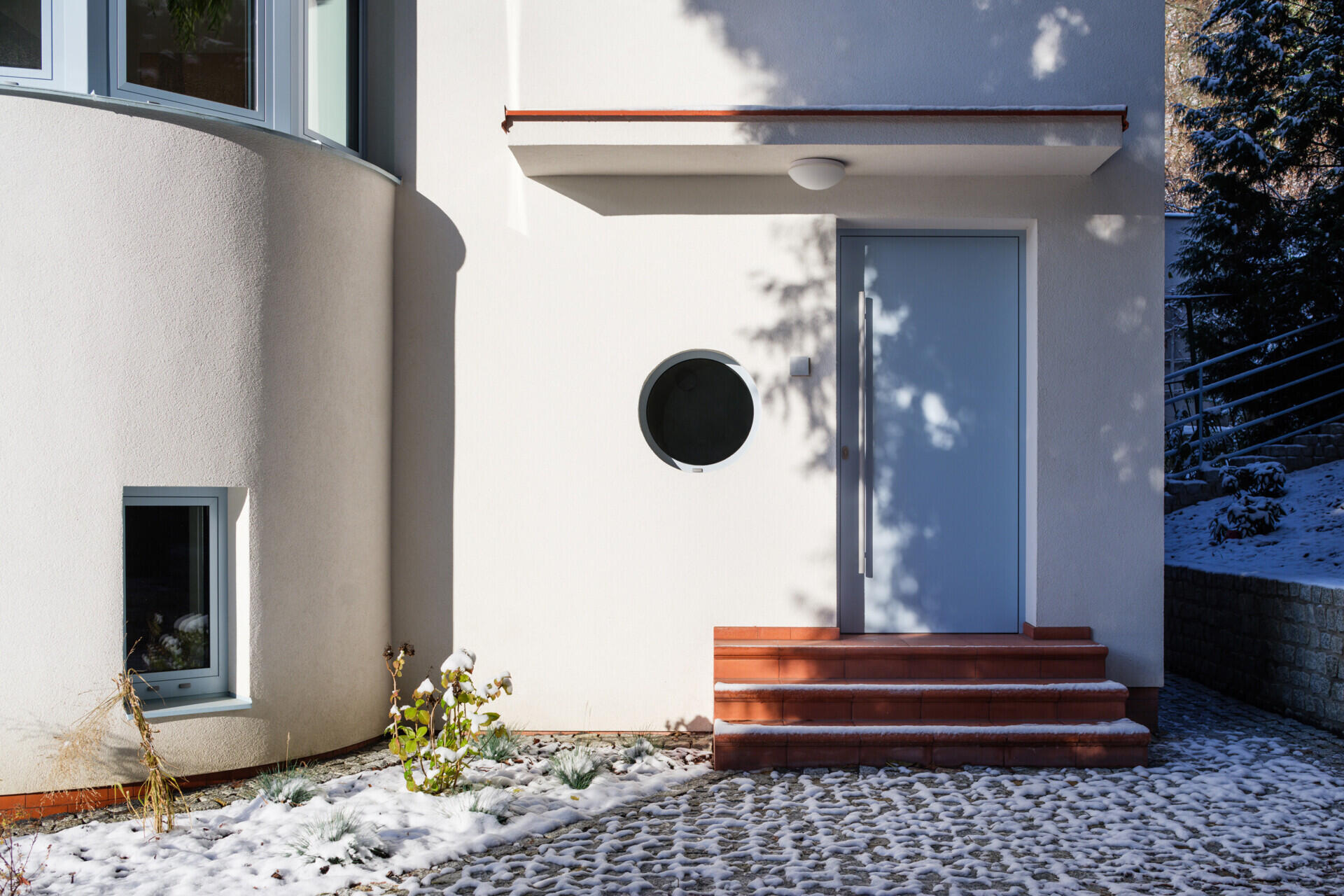 Discover the exterior transformation of Blue Window House in Prague, Czech Republic, by No Architects. The renovated modernist home features a white facade, curved window bays, distinctive blue aluminum window frames, and a redesigned garden.