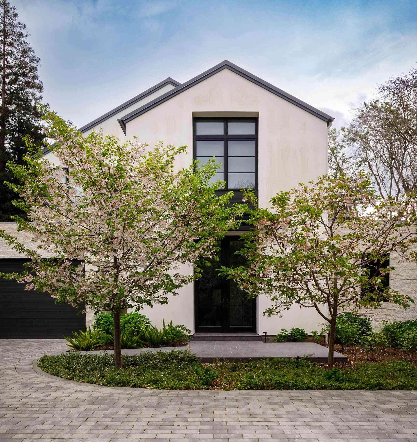 Tour the exterior and backyard of the Atherton Residence by SDG Architecture, where pale gabled volumes, black-framed windows, stone accents, mature landscaping and a large pool create a clean contemporary setting.