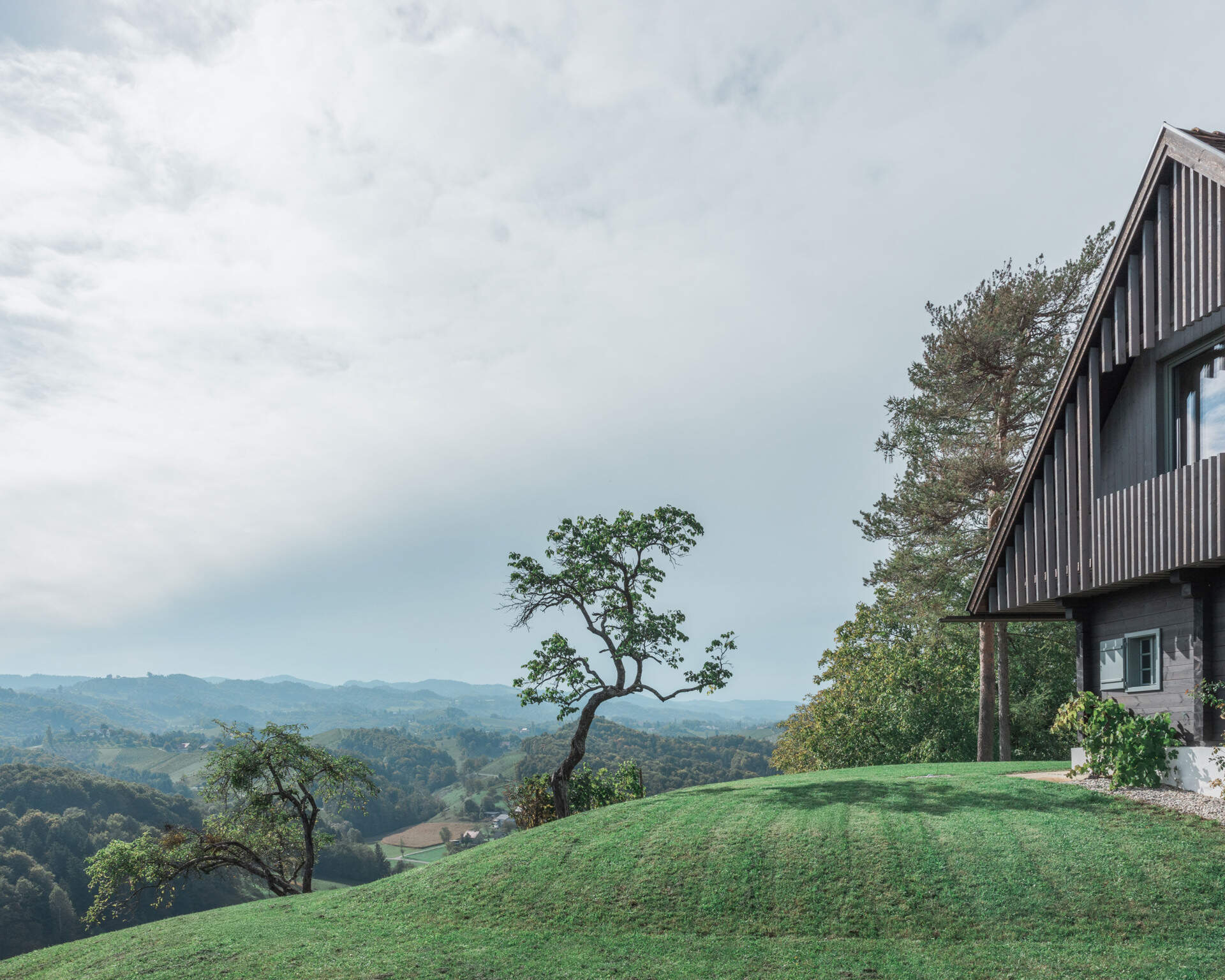 Traditional farmhouse architecture meets contemporary design in this Austrian home renovation, featuring timber screens, a pitched tile roof, modern glazing, and countryside views.
