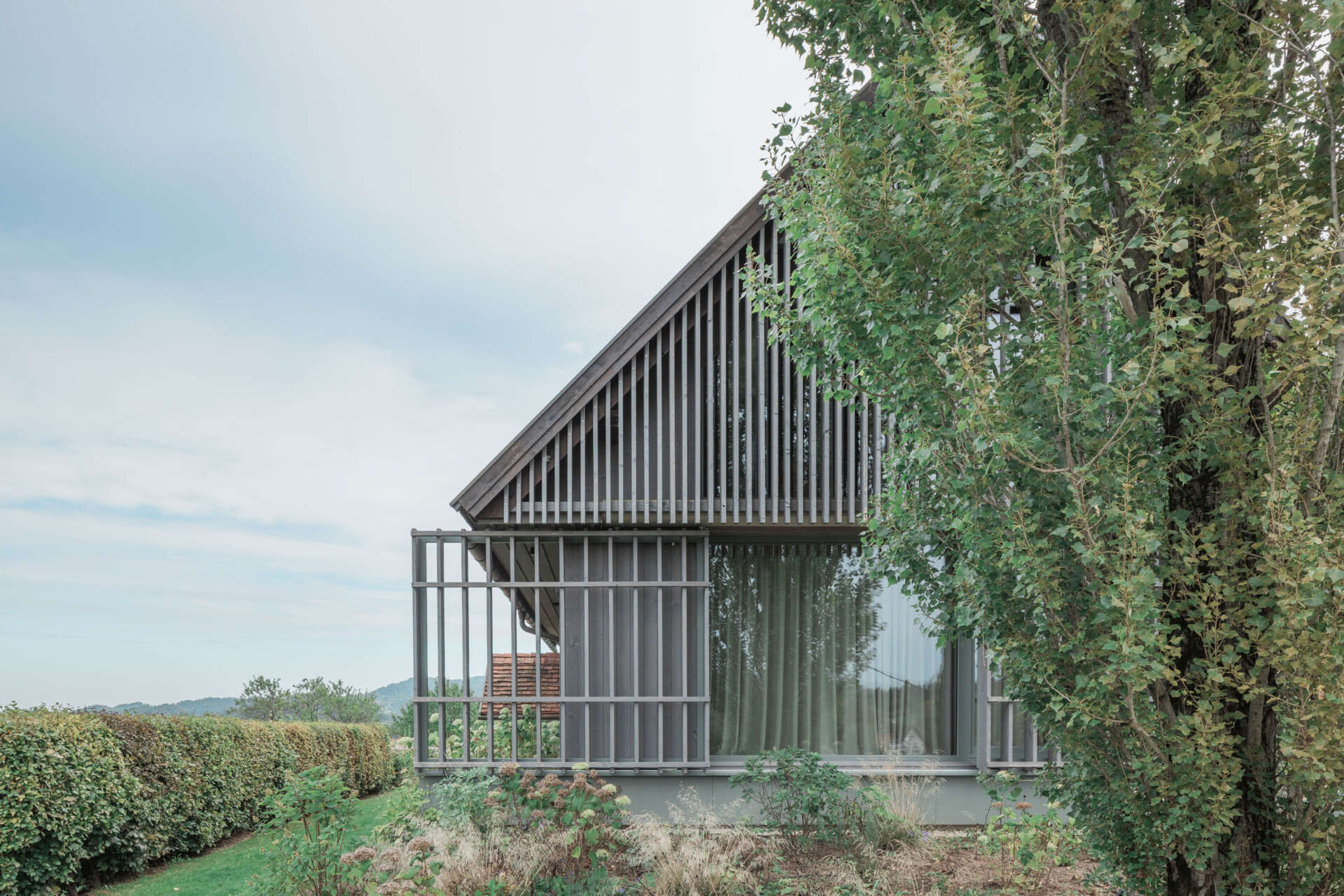 Traditional farmhouse architecture meets contemporary design in this Austrian home renovation, featuring timber screens, a pitched tile roof, modern glazing, and countryside views.