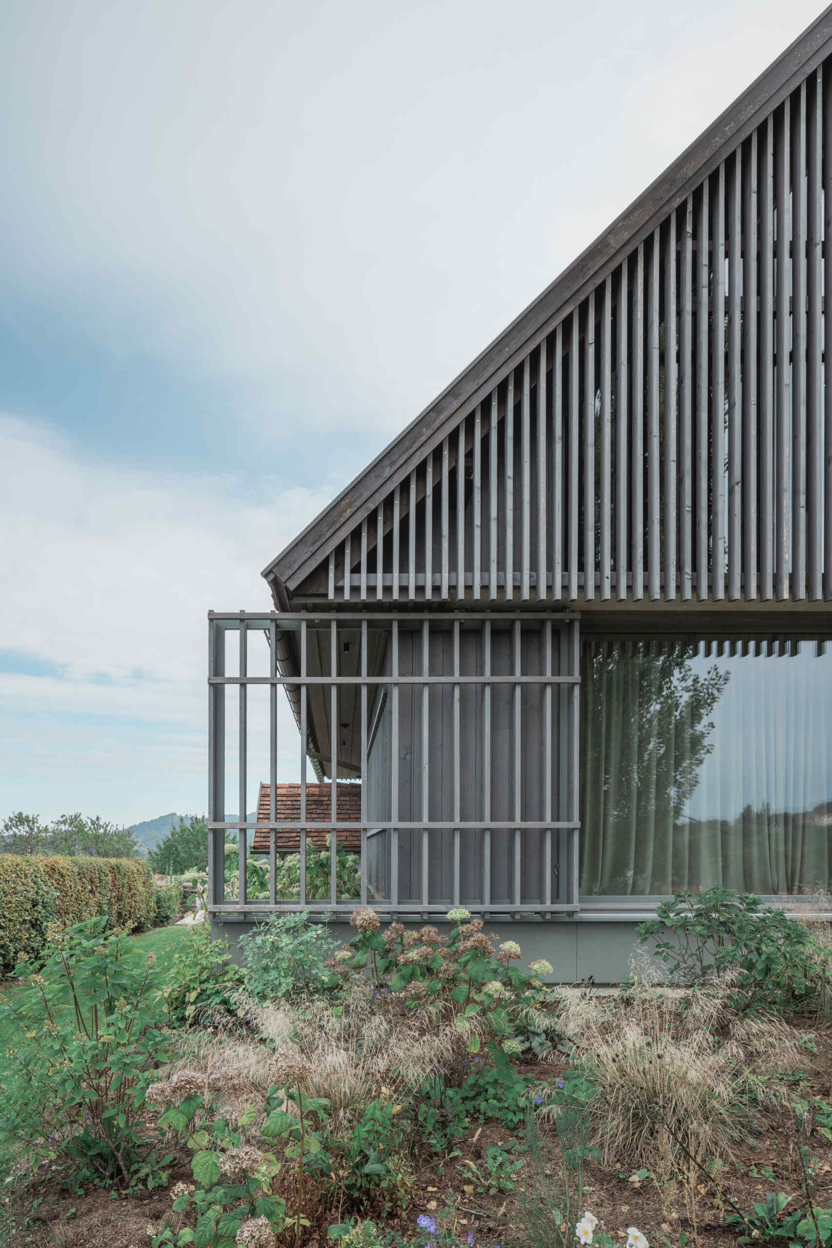 Traditional farmhouse architecture meets contemporary design in this Austrian home renovation, featuring timber screens, a pitched tile roof, modern glazing, and countryside views.