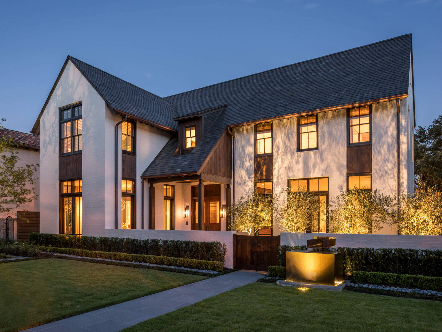 Explore a contemporary house in Houston with white painted brick, steep gabled roofs, redwood siding, dark-framed windows, and landscaped gardens inspired by traditional cottage architecture.