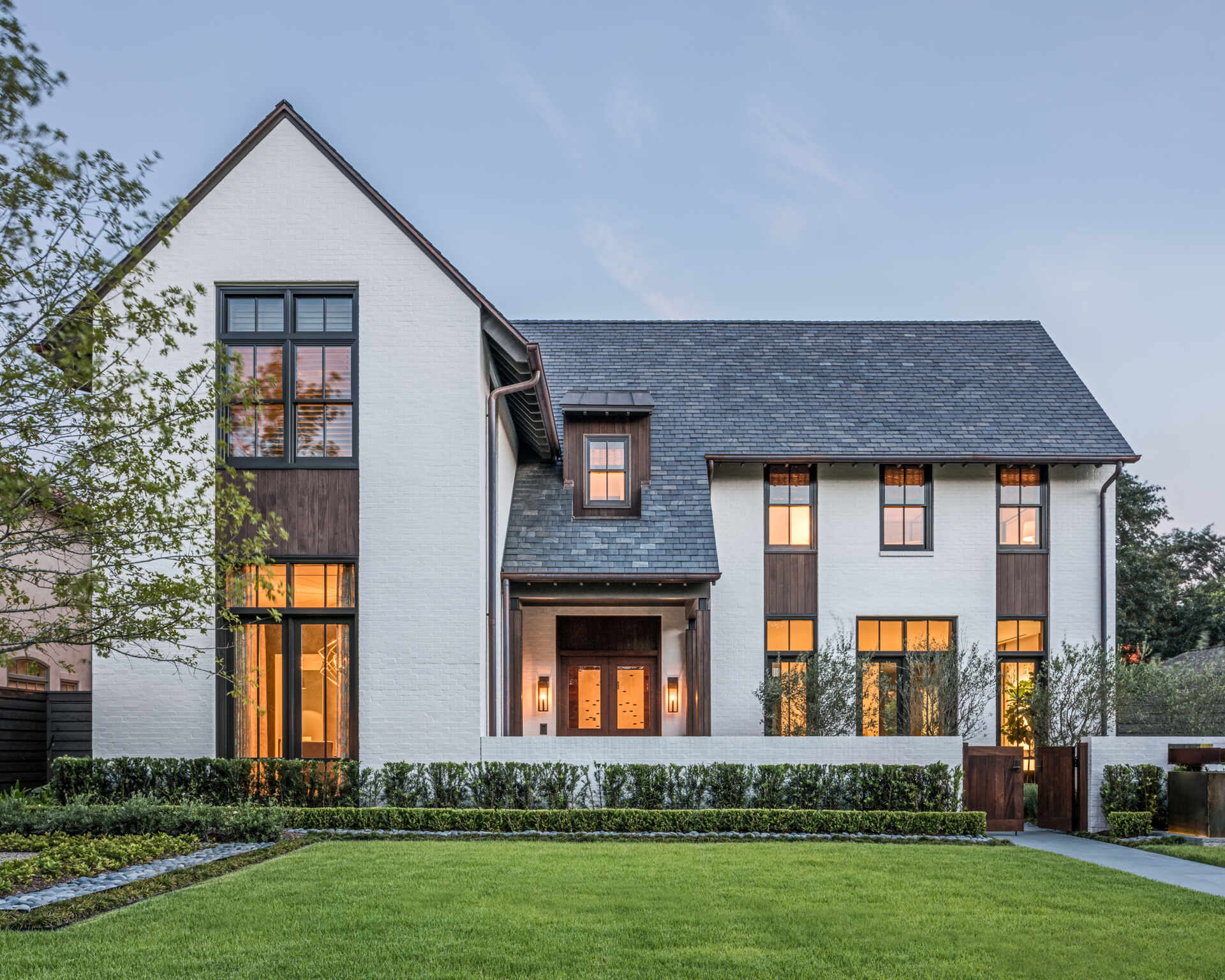 Explore a contemporary house in Houston with white painted brick, steep gabled roofs, redwood siding, dark-framed windows, and landscaped gardens inspired by traditional cottage architecture.