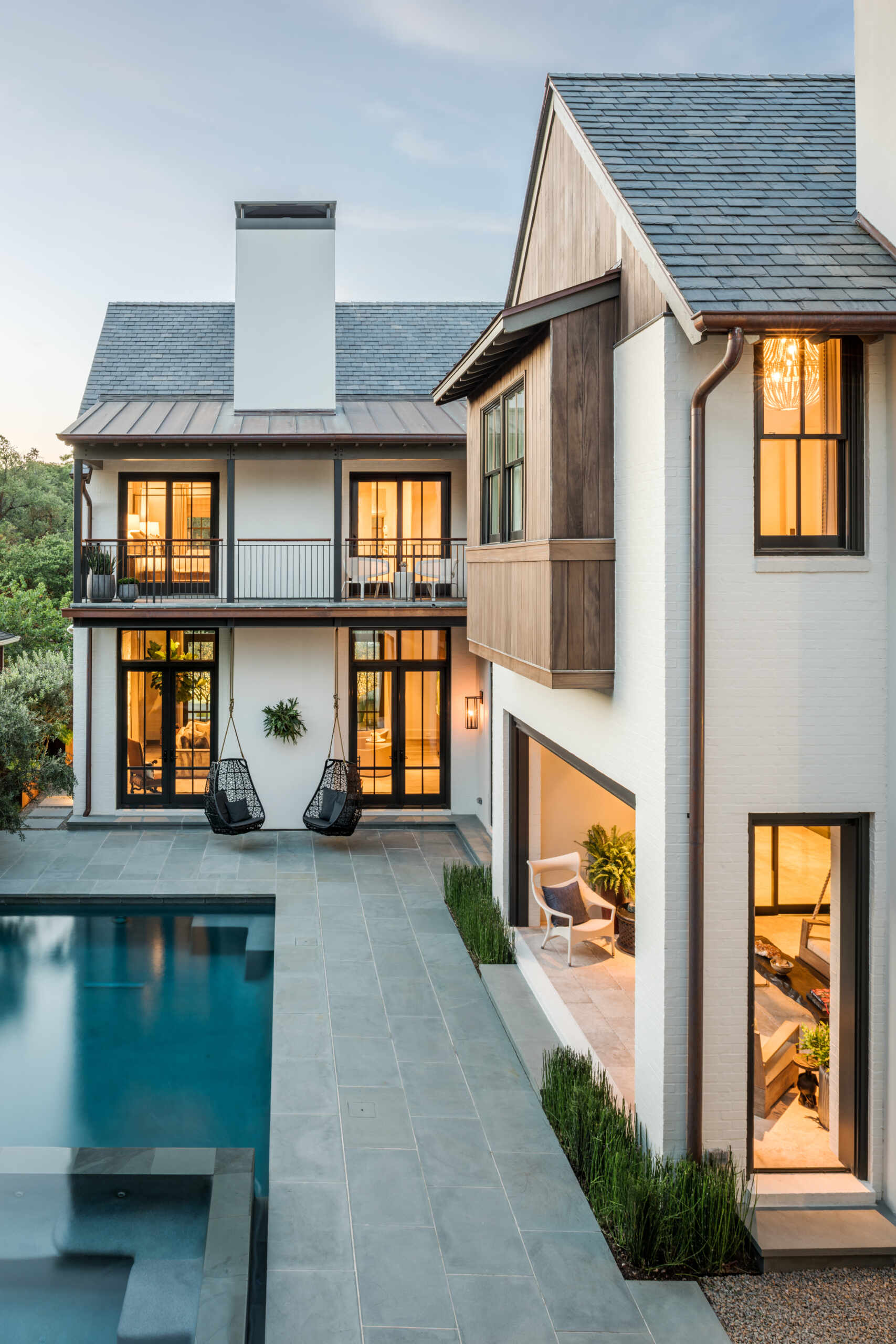 A contemporary Houston courtyard with a rectangular swimming pool, gray stone paving, hanging chairs, landscaped seating areas, and a two-story outdoor bridge connecting the buildings.