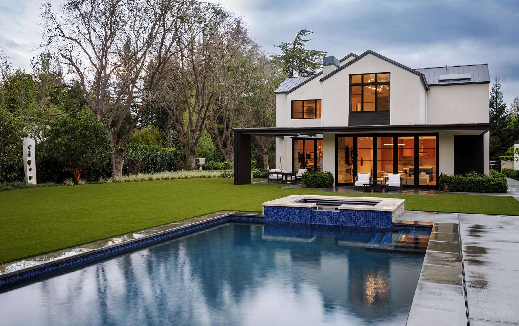 Tour the exterior and backyard of the Atherton Residence by SDG Architecture, where pale gabled volumes, black-framed windows, stone accents, mature landscaping and a large pool create a clean contemporary setting.