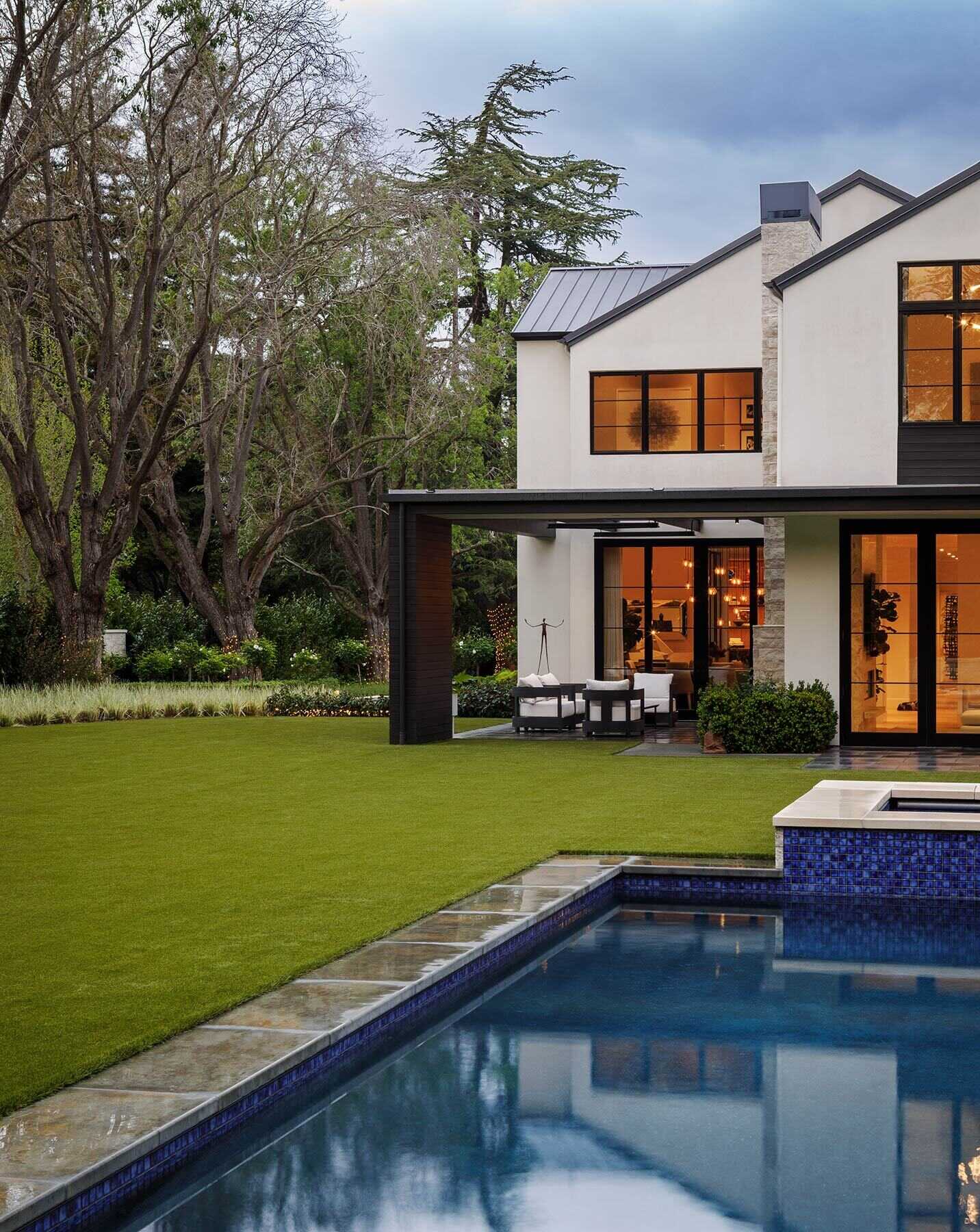 Tour the exterior and backyard of the Atherton Residence by SDG Architecture, where pale gabled volumes, black-framed windows, stone accents, mature landscaping and a large pool create a clean contemporary setting.