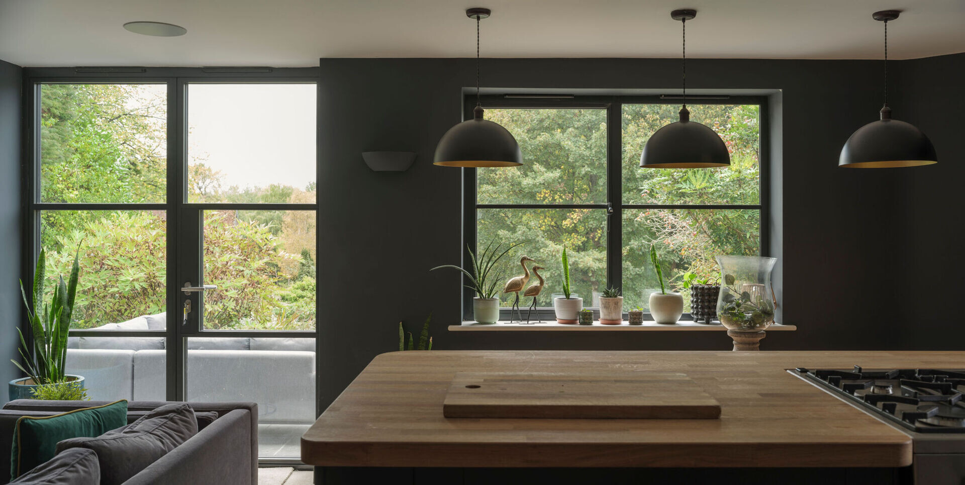 An open-plan kitchen and dining area pairs dark cabinets, natural wood countertops, a kitchen island, and rustic exposed brick arches in a renovated English cottage.