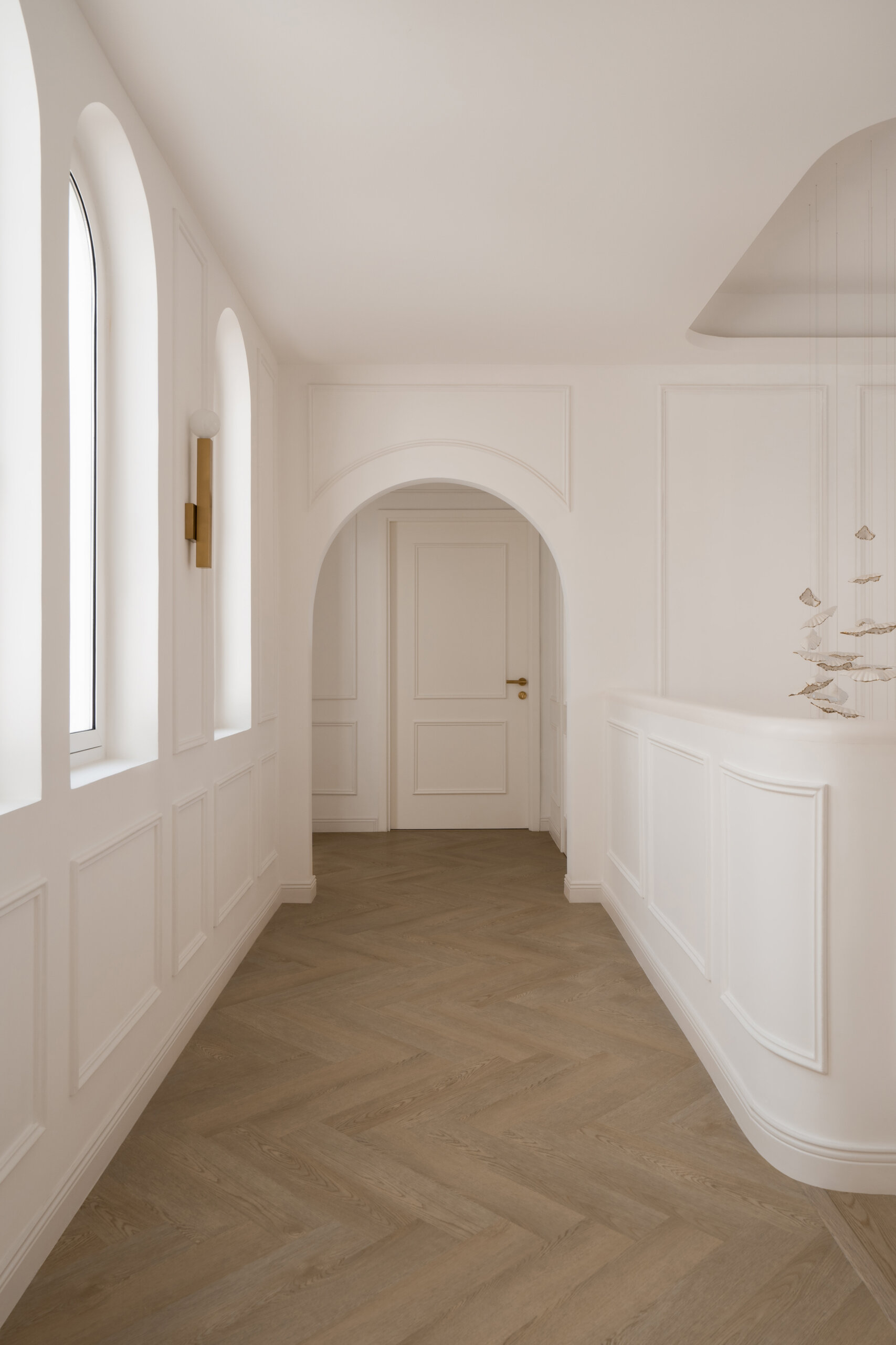 Explore the elegant upper hallway inside The White Arcade by D’Ora Tokai Designs. Featuring arched windows, white wall mouldings, pale oak flooring, and brass wall lights, this Dubai villa showcases beautiful contemporary architecture.