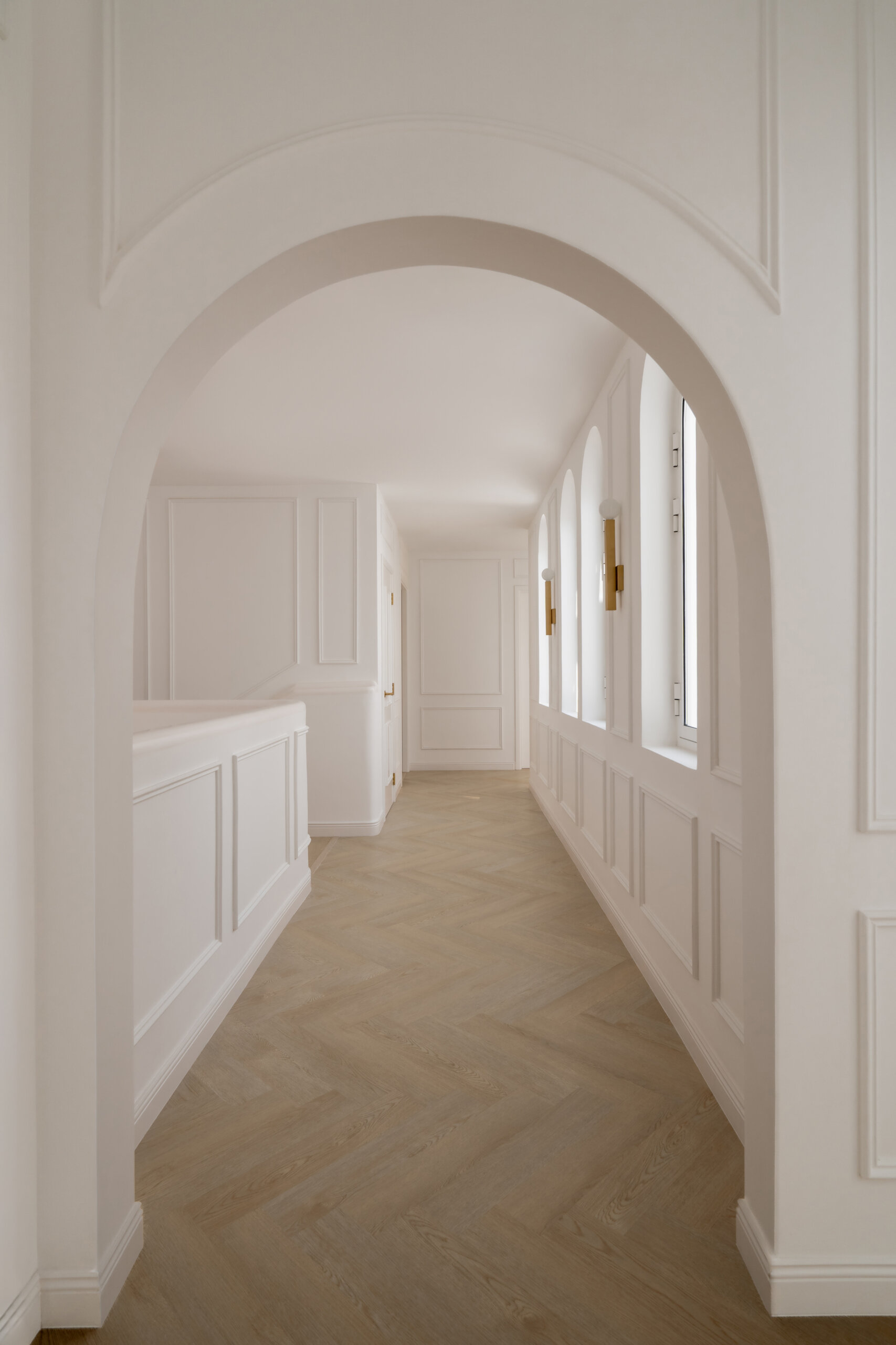 Explore the elegant upper hallway inside The White Arcade by D’Ora Tokai Designs. Featuring arched windows, white wall mouldings, pale oak flooring, and brass wall lights, this Dubai villa showcases beautiful contemporary architecture.