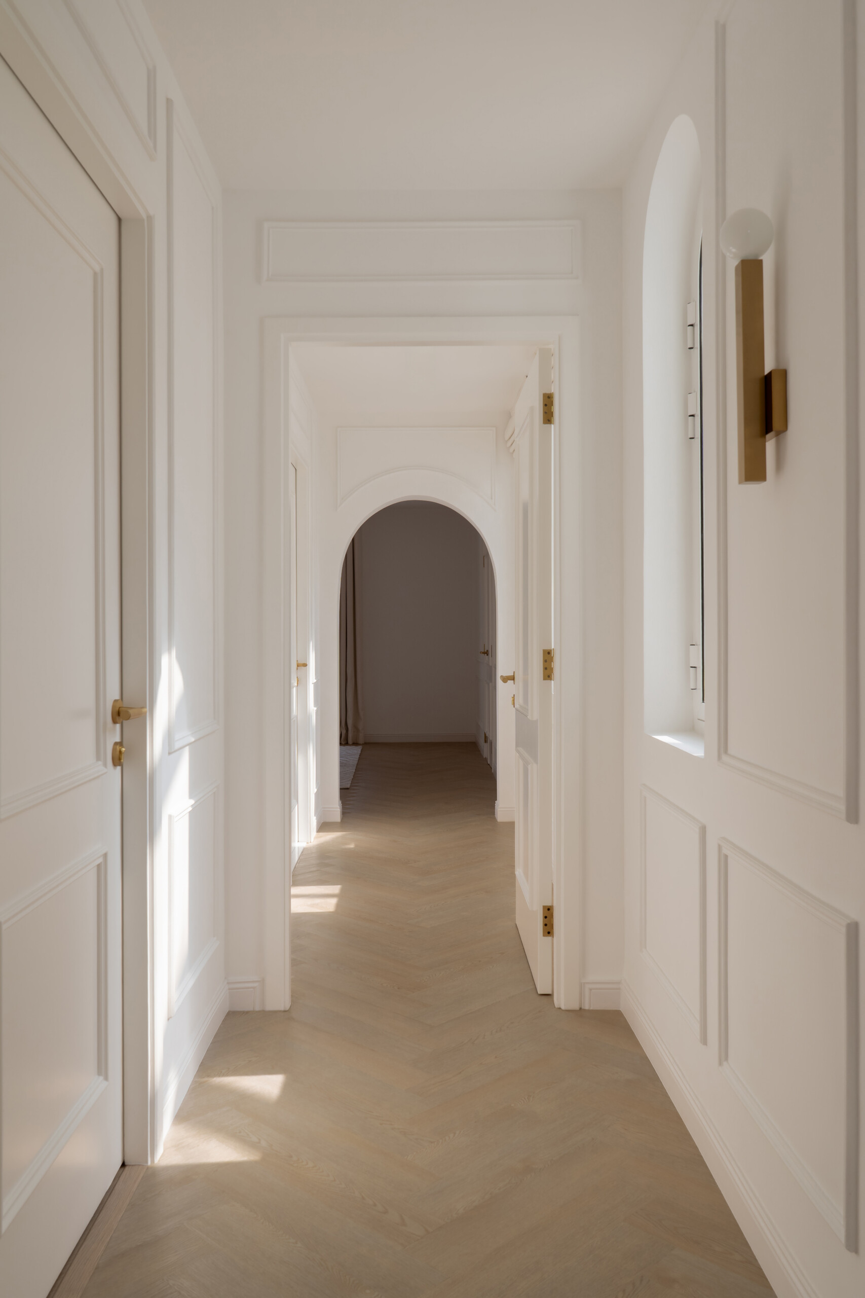 Explore the elegant upper hallway inside The White Arcade by D’Ora Tokai Designs. Featuring arched windows, white wall mouldings, pale oak flooring, and brass wall lights, this Dubai villa showcases beautiful contemporary architecture.