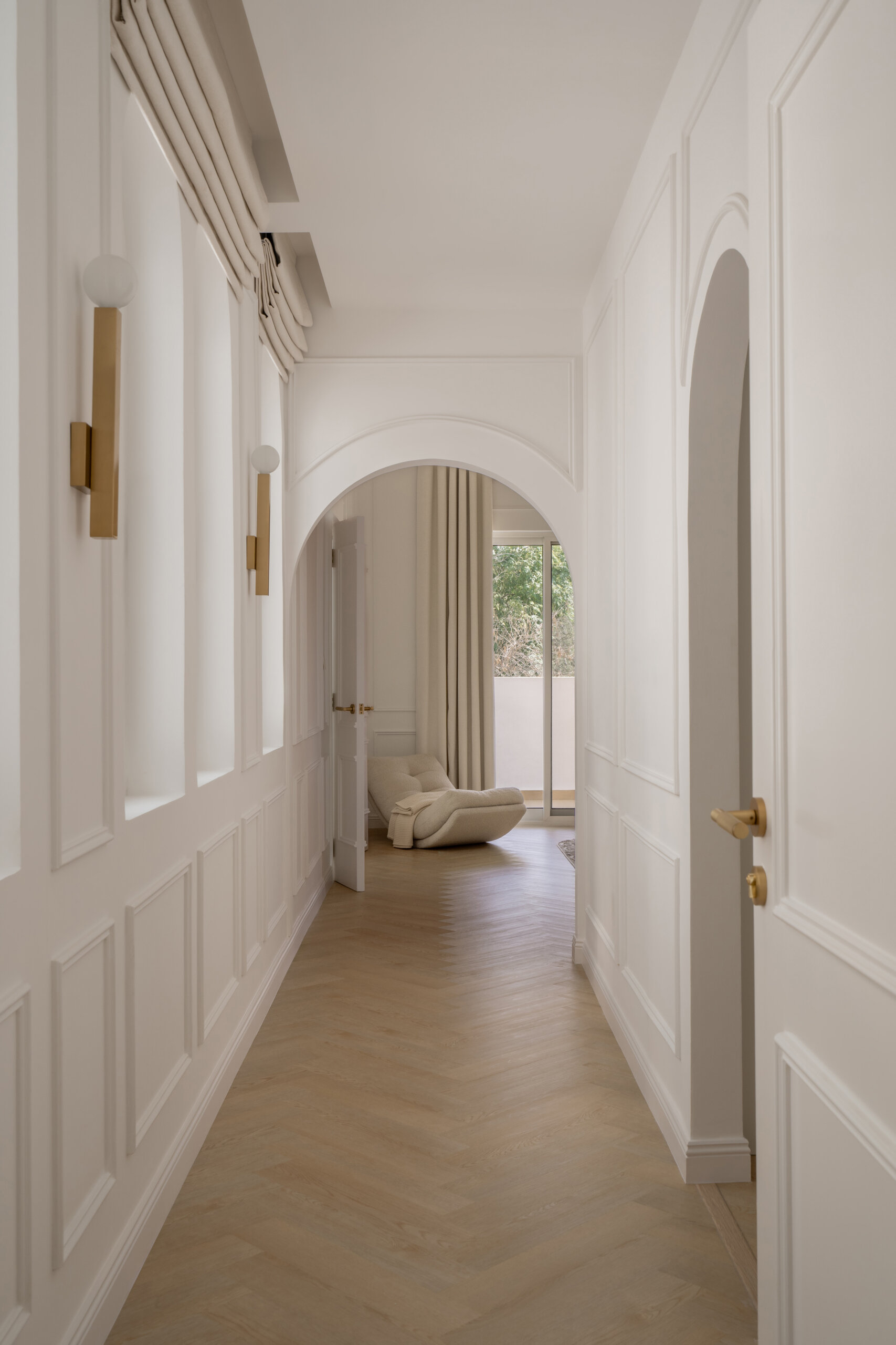 Explore the elegant upper hallway inside The White Arcade by D’Ora Tokai Designs. Featuring arched windows, white wall mouldings, pale oak flooring, and brass wall lights, this Dubai villa showcases beautiful contemporary architecture.