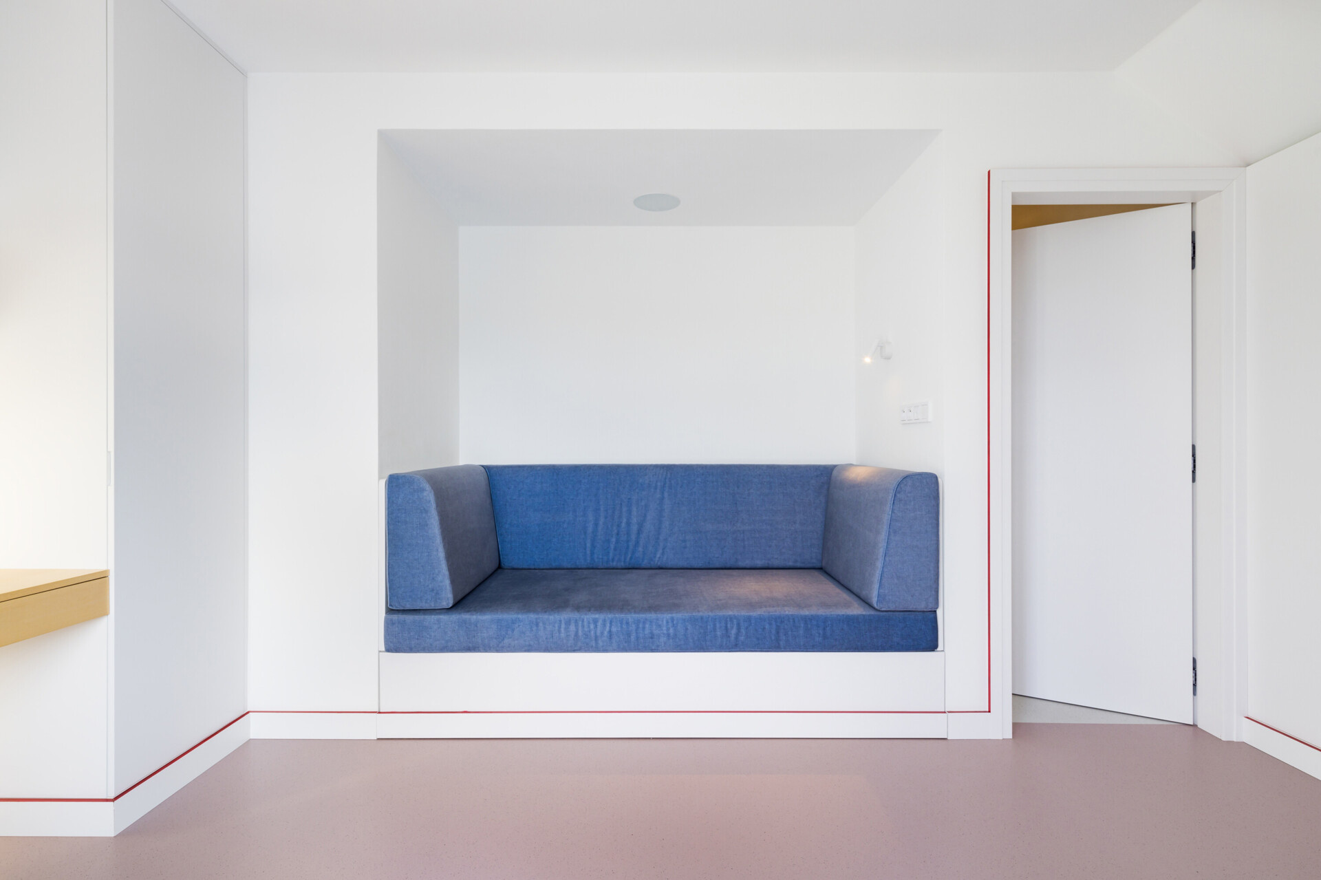 Explore the contemporary bedroom designs inside Blue Window House, featuring vertical timber wall panels, custom wooden wardrobes, integrated bedside shelves, and subtle lighting. Natural wood finishes and a red upholstered bed frame bring warmth and color to the minimalist interiors.