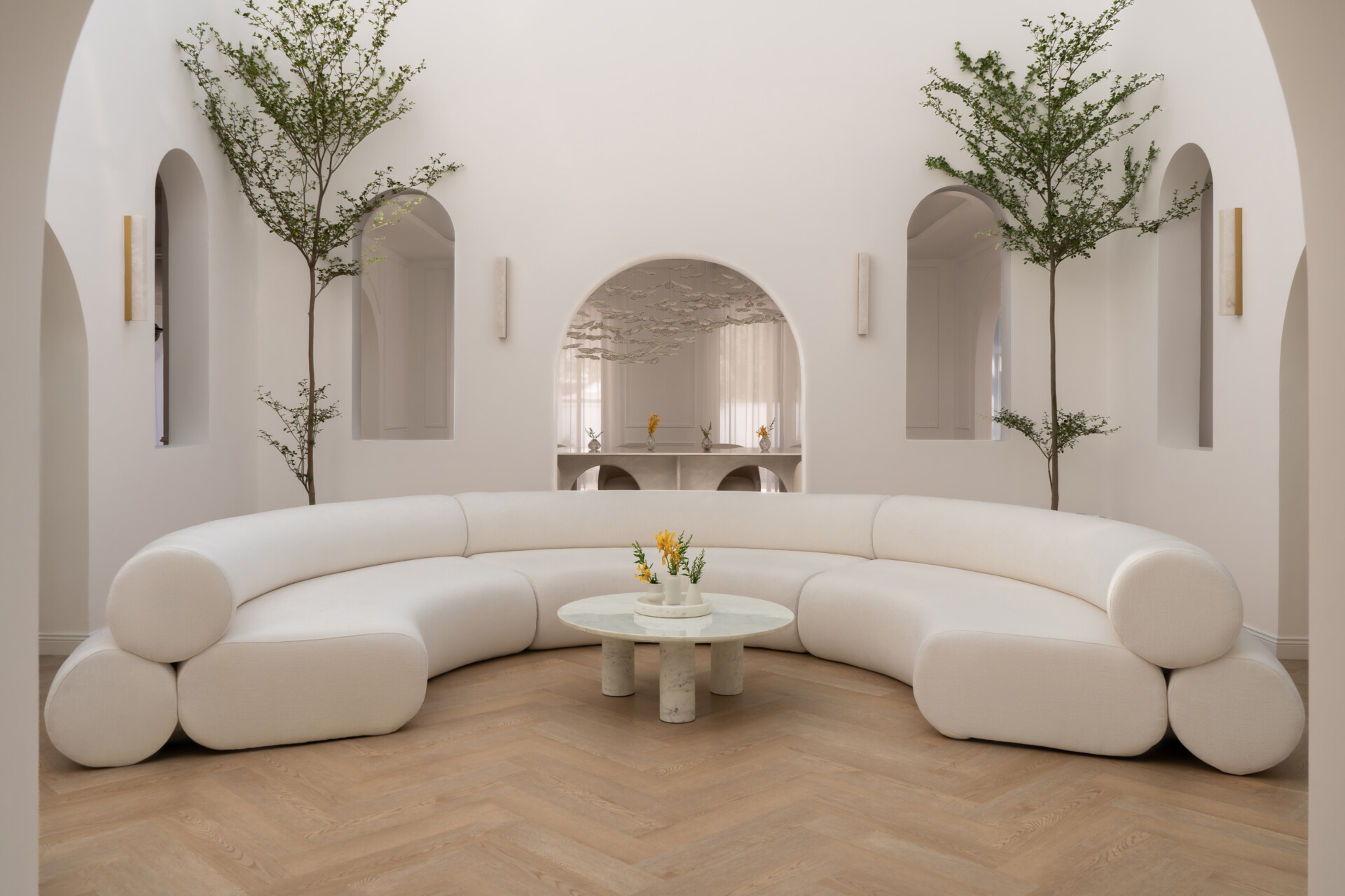 Discover the central courtyard inside The White Arcade, a Dubai villa renovated by D’Ora Tokai Designs. Featuring double-height ceilings, a glass roof, sculptural arches, a bespoke C-shaped sofa, indoor trees, and a floating leaf installation, this unique living space is filled with natural light.