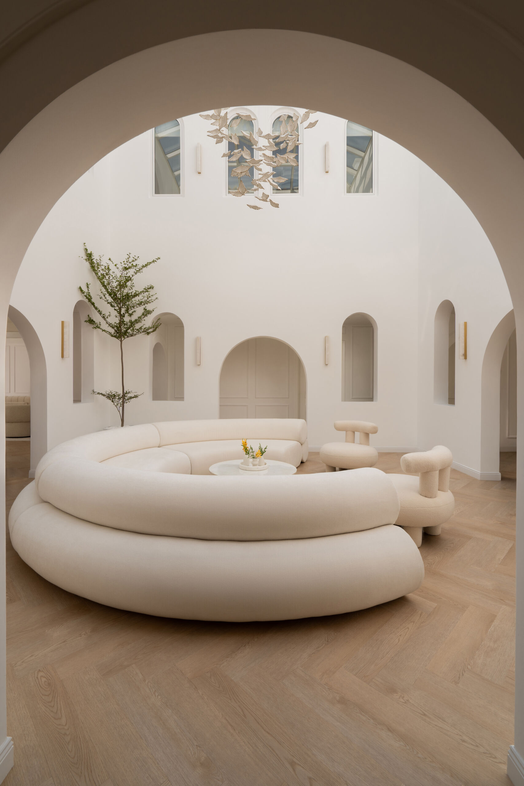 Discover the central courtyard inside The White Arcade, a Dubai villa renovated by D’Ora Tokai Designs. Featuring double-height ceilings, a glass roof, sculptural arches, a bespoke C-shaped sofa, indoor trees, and a floating leaf installation, this unique living space is filled with natural light.