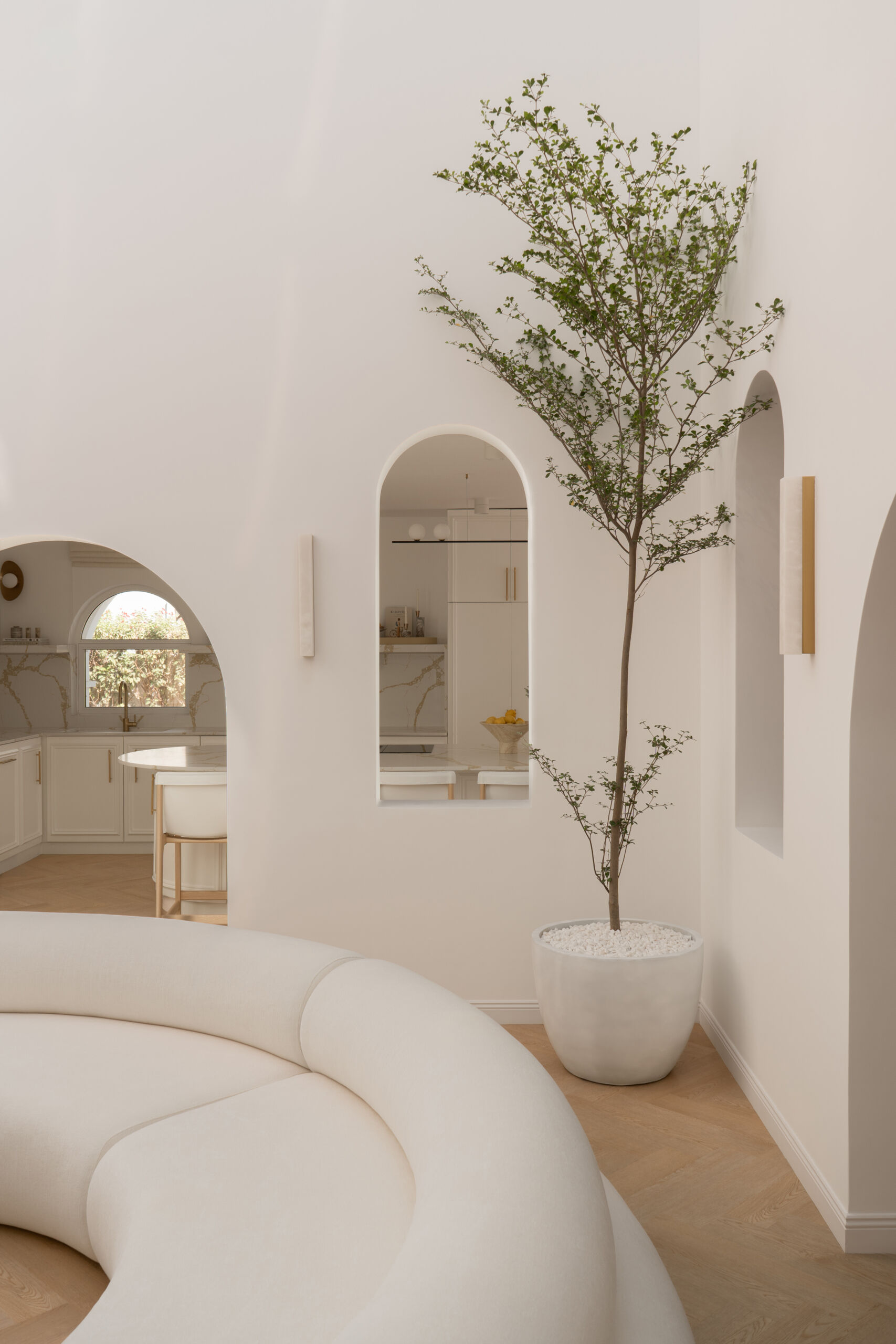 Discover the central courtyard inside The White Arcade, a Dubai villa renovated by D’Ora Tokai Designs. Featuring double-height ceilings, a glass roof, sculptural arches, a bespoke C-shaped sofa, indoor trees, and a floating leaf installation, this unique living space is filled with natural light.