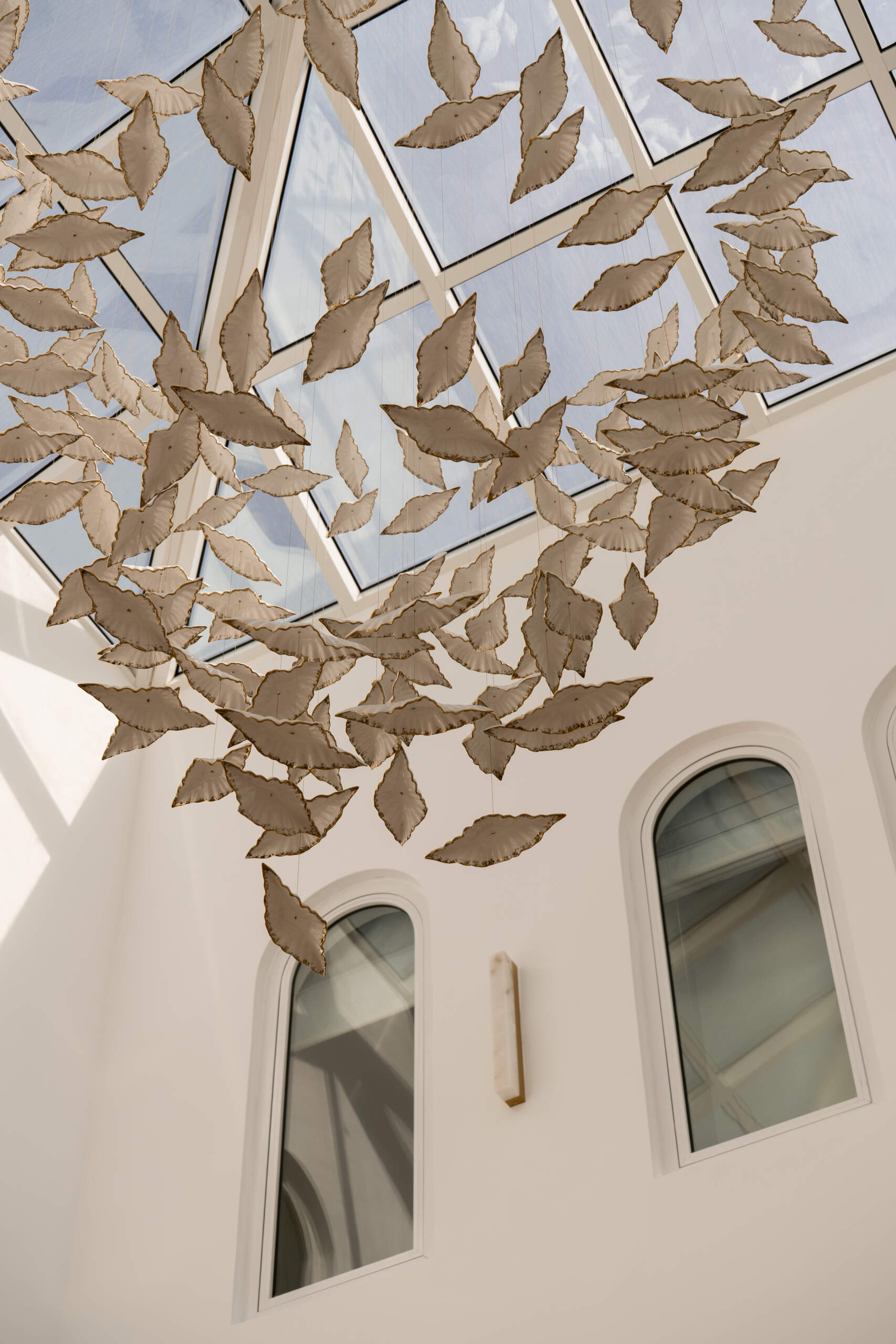 Discover the central courtyard inside The White Arcade, a Dubai villa renovated by D’Ora Tokai Designs. Featuring double-height ceilings, a glass roof, sculptural arches, a bespoke C-shaped sofa, indoor trees, and a floating leaf installation, this unique living space is filled with natural light.