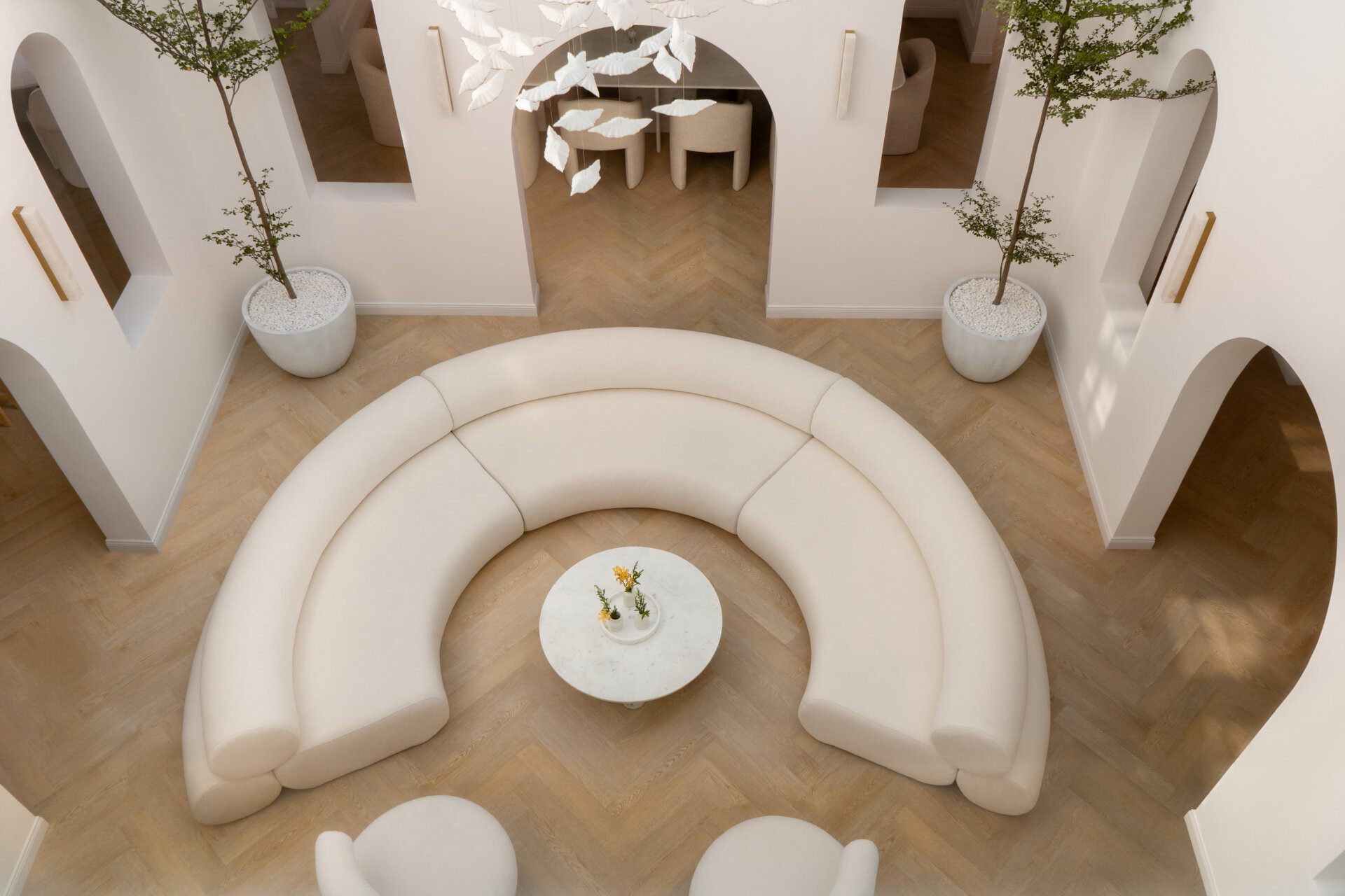 Discover the central courtyard inside The White Arcade, a Dubai villa renovated by D’Ora Tokai Designs. Featuring double-height ceilings, a glass roof, sculptural arches, a bespoke C-shaped sofa, indoor trees, and a floating leaf installation, this unique living space is filled with natural light.