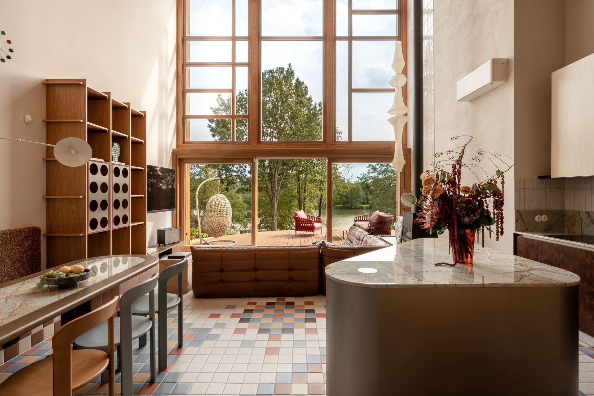 Contemporary kitchen inspiration featuring rich burl wood cabinets, Aurora Borealis quartzite countertops, cream vertical tiles, and a curved metal kitchen island in a colorful Polish lakeside home.