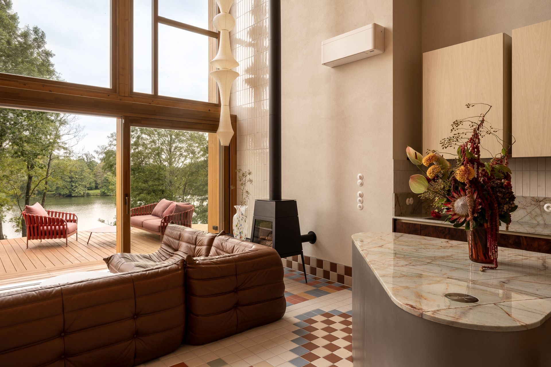 Contemporary kitchen inspiration featuring rich burl wood cabinets, Aurora Borealis quartzite countertops, cream vertical tiles, and a curved metal kitchen island in a colorful Polish lakeside home.