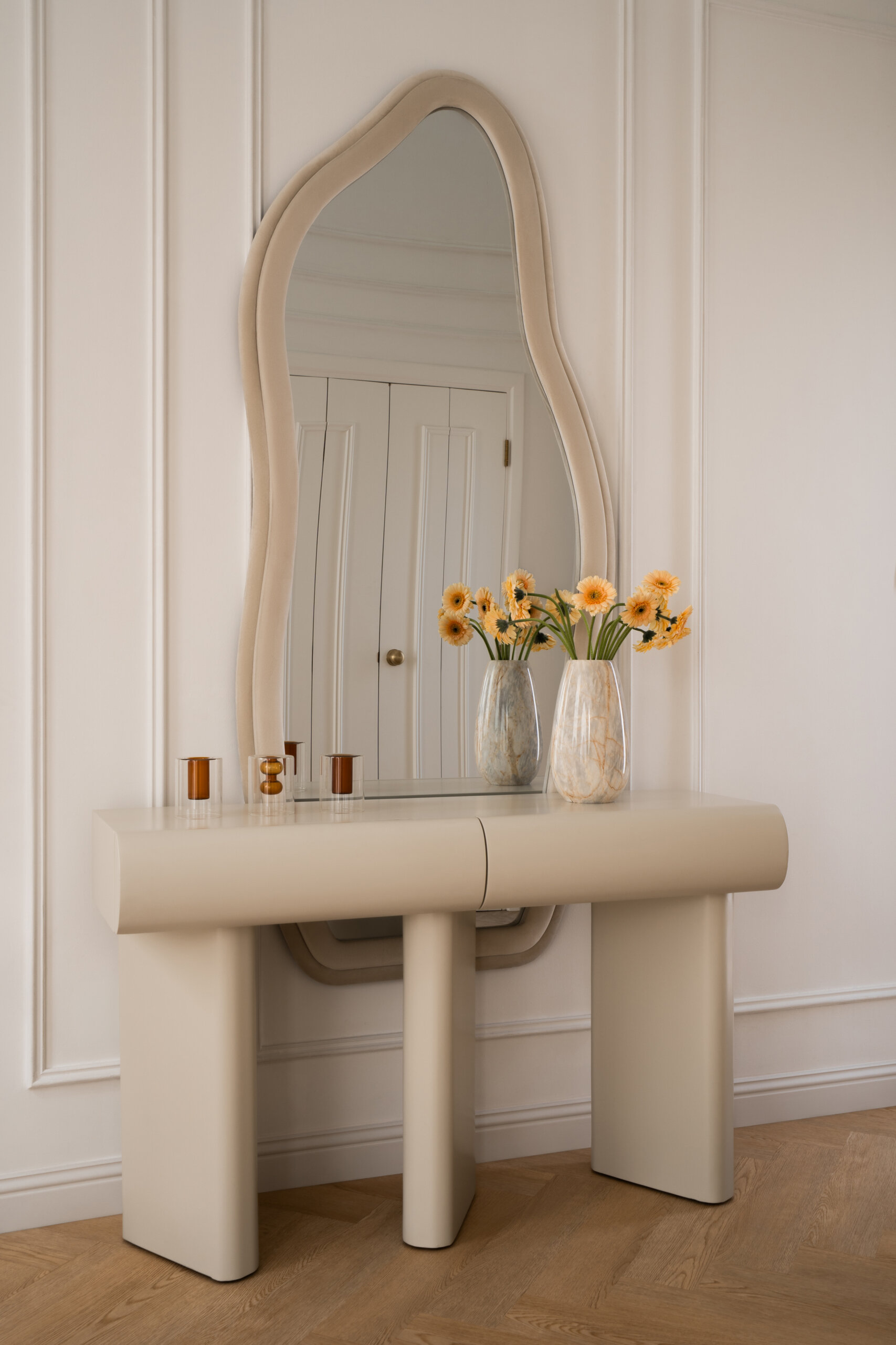 A beautiful neutral entryway inside The White Arcade by D’Ora Tokai Designs. Featuring a sculptural cream console table, an organic-shaped mirror, elegant wall panelling, and light oak herringbone flooring, this Dubai home offers plenty of inspiration for contemporary entrance design.