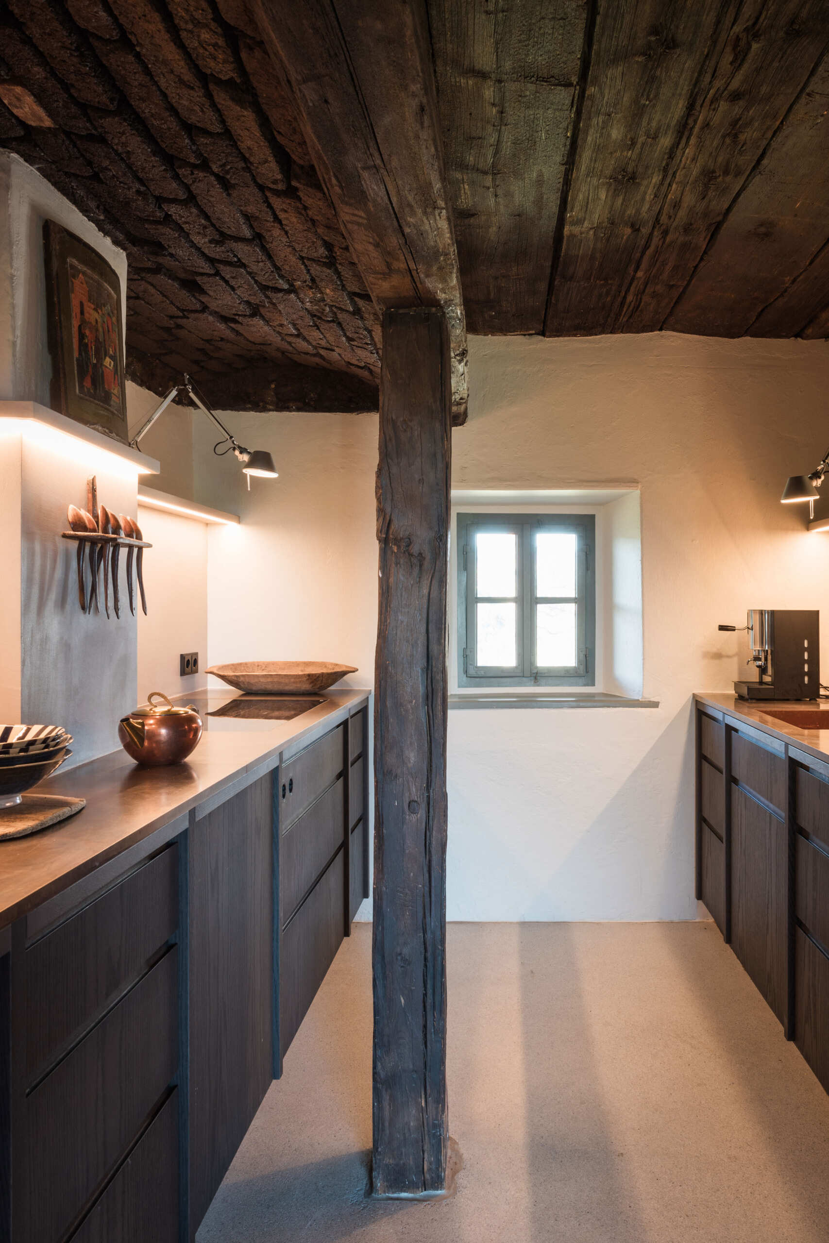 This Austrian farmhouse kitchen pairs an original vaulted brick ceiling and exposed timber beams with dark wood cabinets, modern lighting, and warm metal countertops.