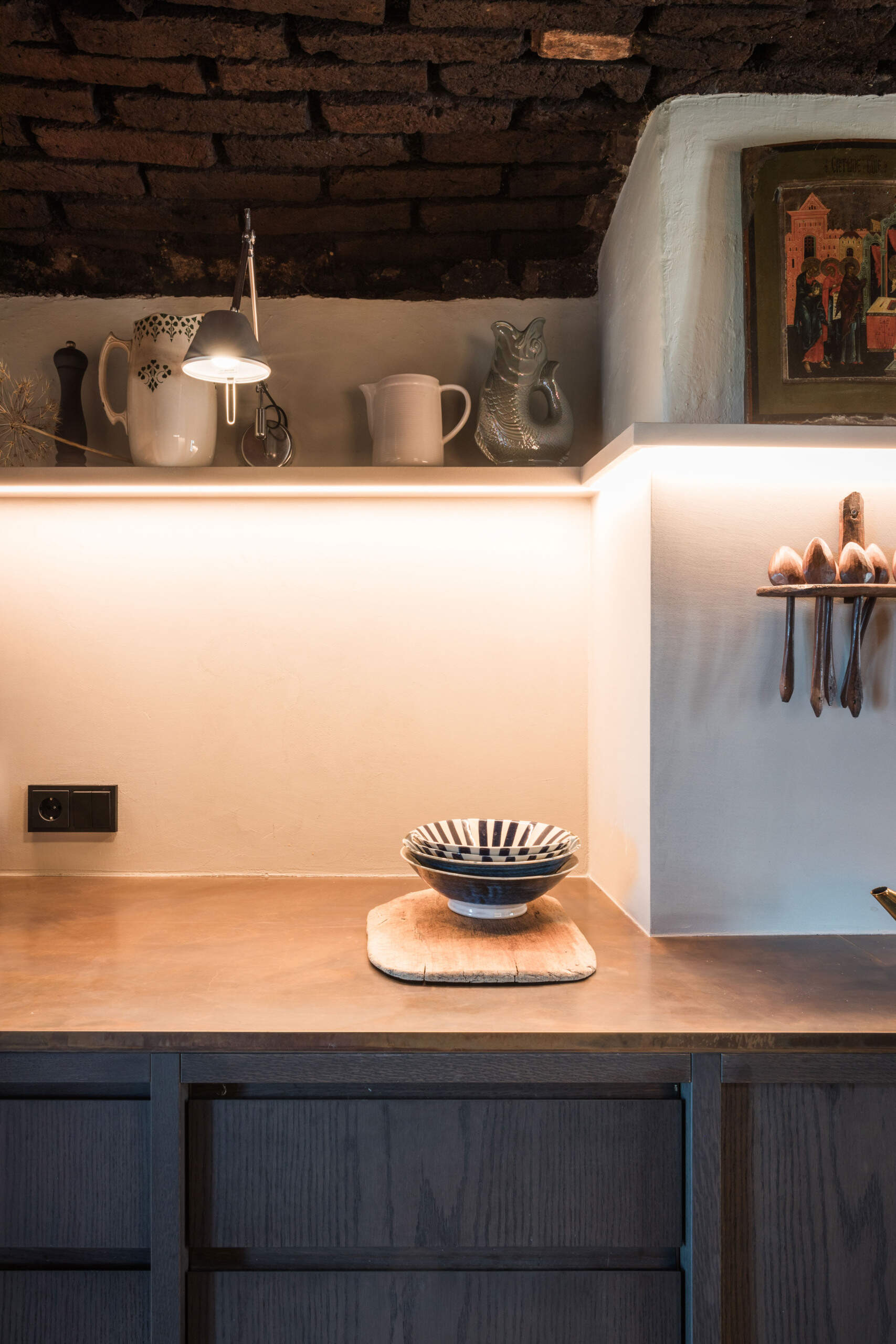 This Austrian farmhouse kitchen pairs an original vaulted brick ceiling and exposed timber beams with dark wood cabinets, modern lighting, and warm metal countertops.