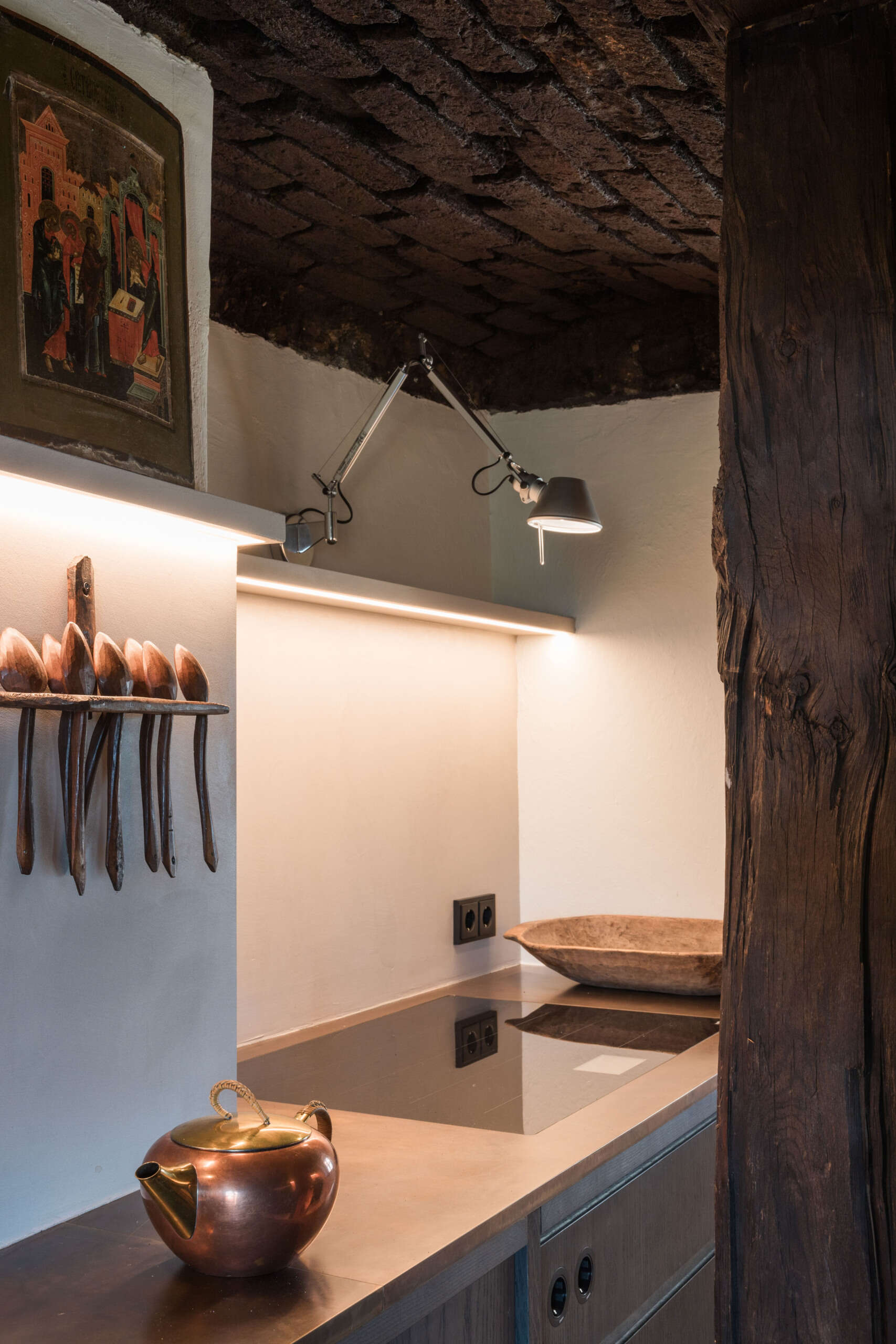 This Austrian farmhouse kitchen pairs an original vaulted brick ceiling and exposed timber beams with dark wood cabinets, modern lighting, and warm metal countertops.