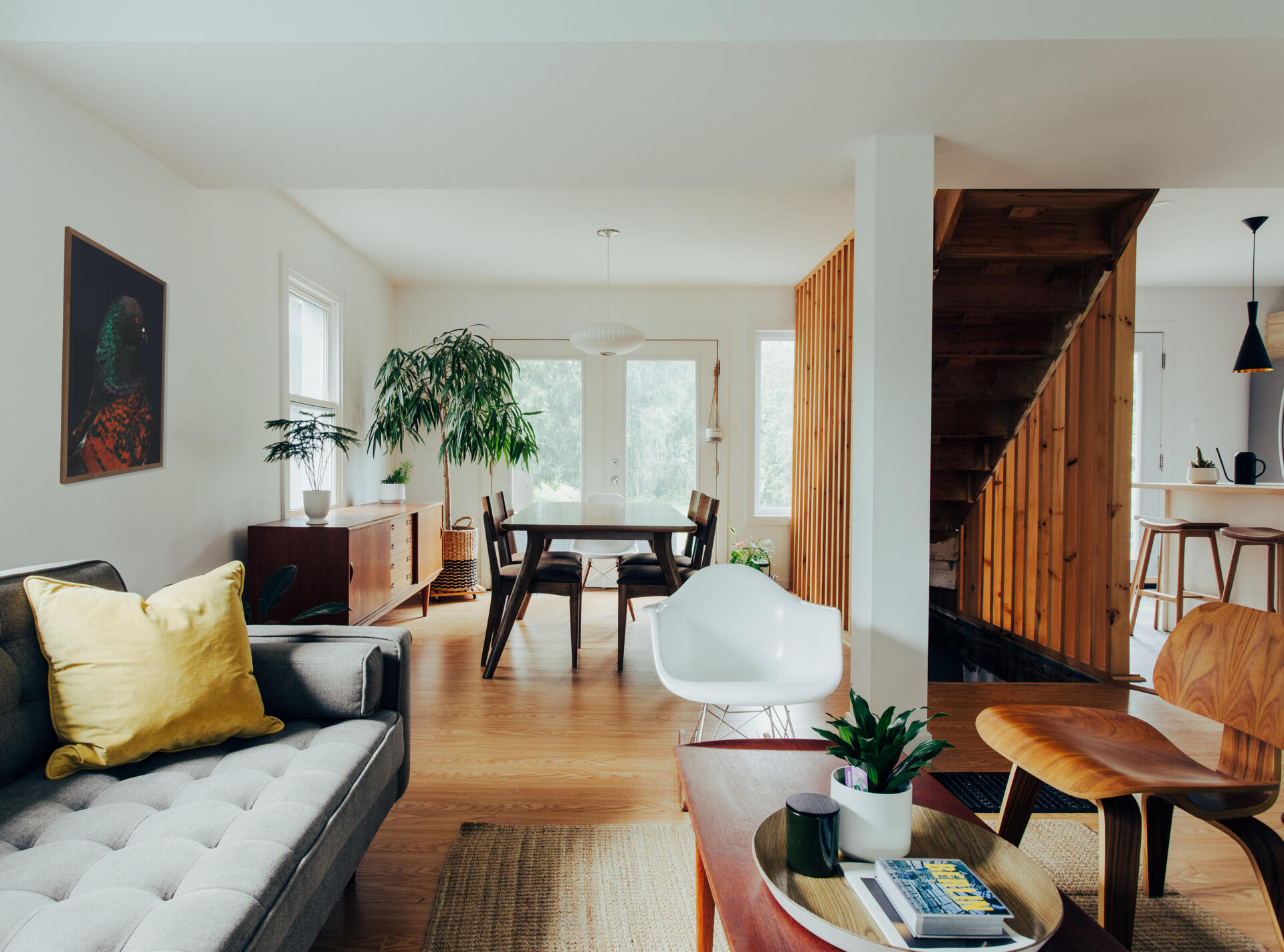 Tour an open-plan living and dining room with warm wood floors, mid-century furniture, white walls, indoor plants, and a simple layout designed for a compact family home.
