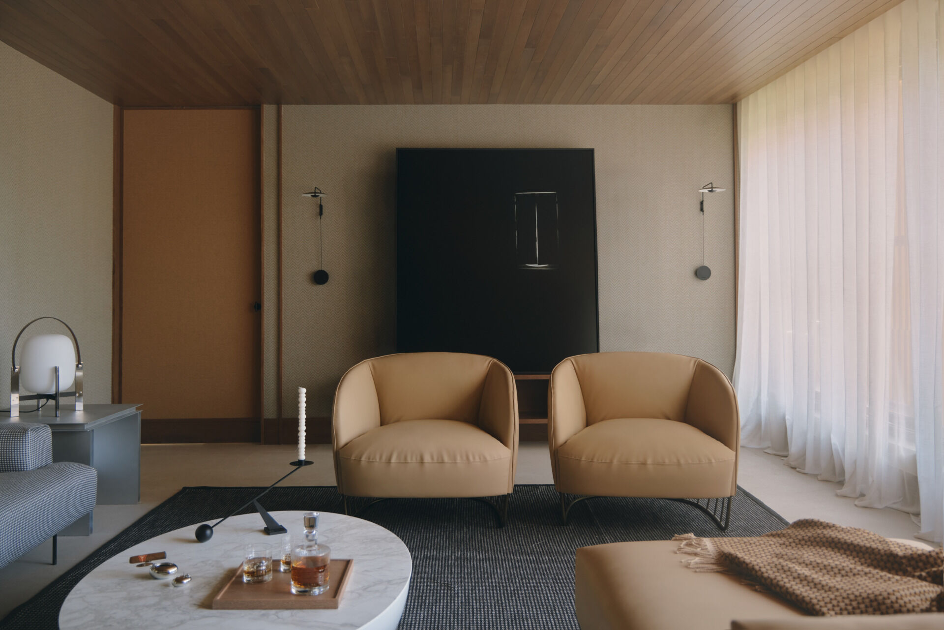 Step inside a contemporary cigar lounge with herringbone wallpaper, a concrete fireplace, caramel-colored lounge chairs, a marble coffee table, and designer lighting.