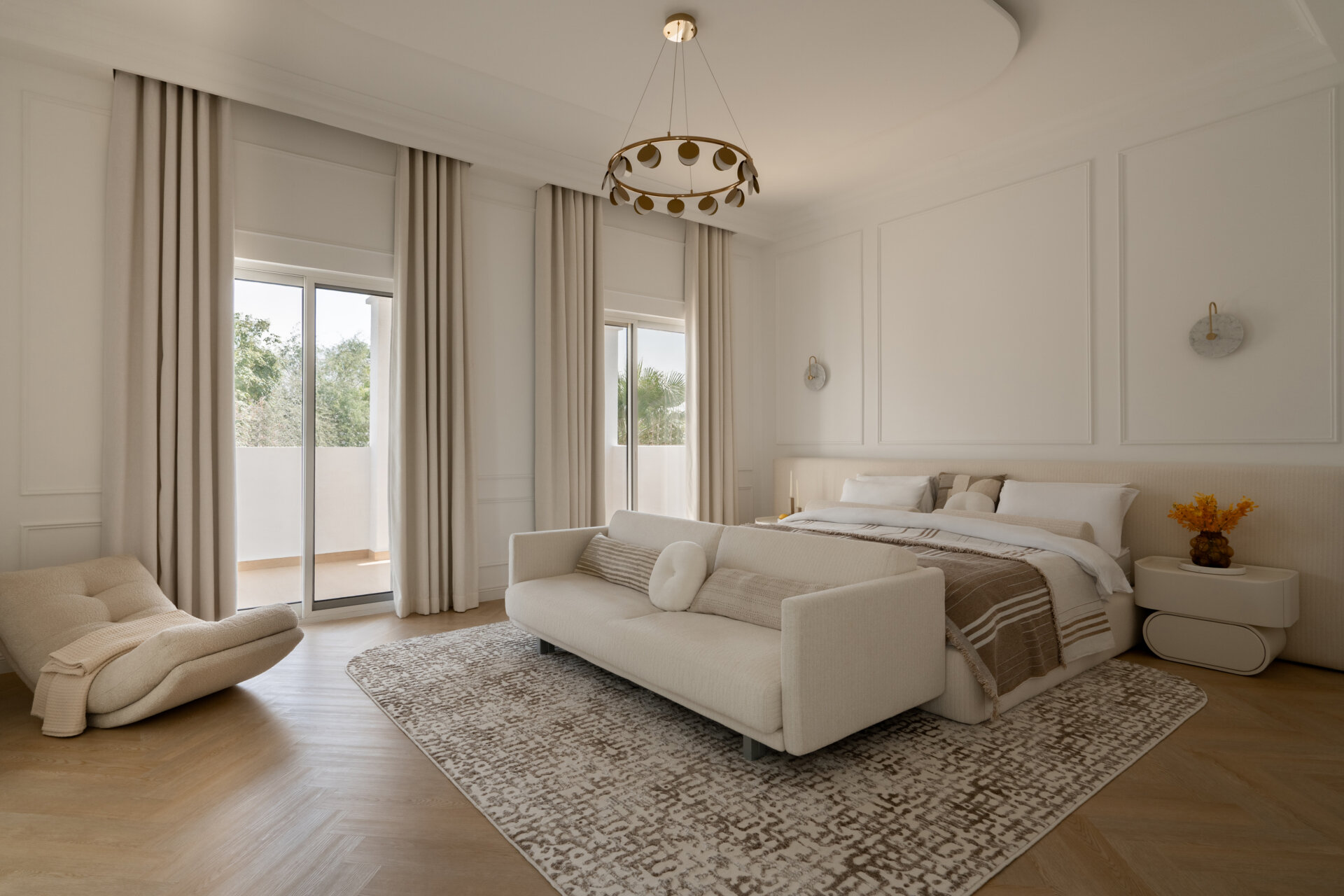 Inside the luxurious primary bedroom of The White Arcade in Dubai, designed by D’Ora Tokai Designs. The spacious suite features a bespoke upholstered bed, cream sofa, sculptural lounge chair, brass chandelier, and soft neutral furnishings with access to a private balcony.