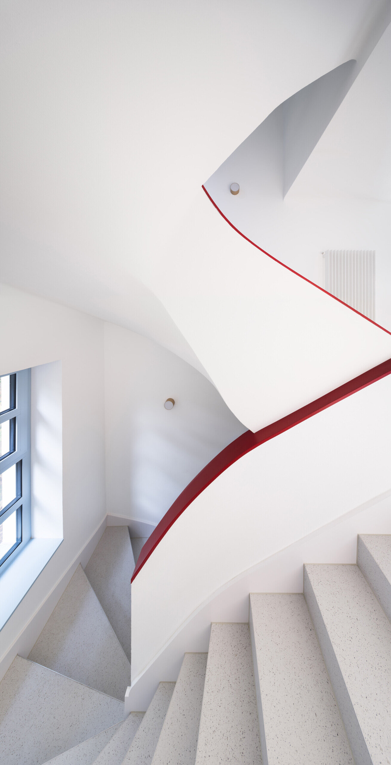 Discover the colorful architectural details inside this modernist house renovation in Prague. A curved staircase with pale blue steps, slender red railings, and subtle red accents along doors, baseboards, and furniture introduces an unexpected design element.