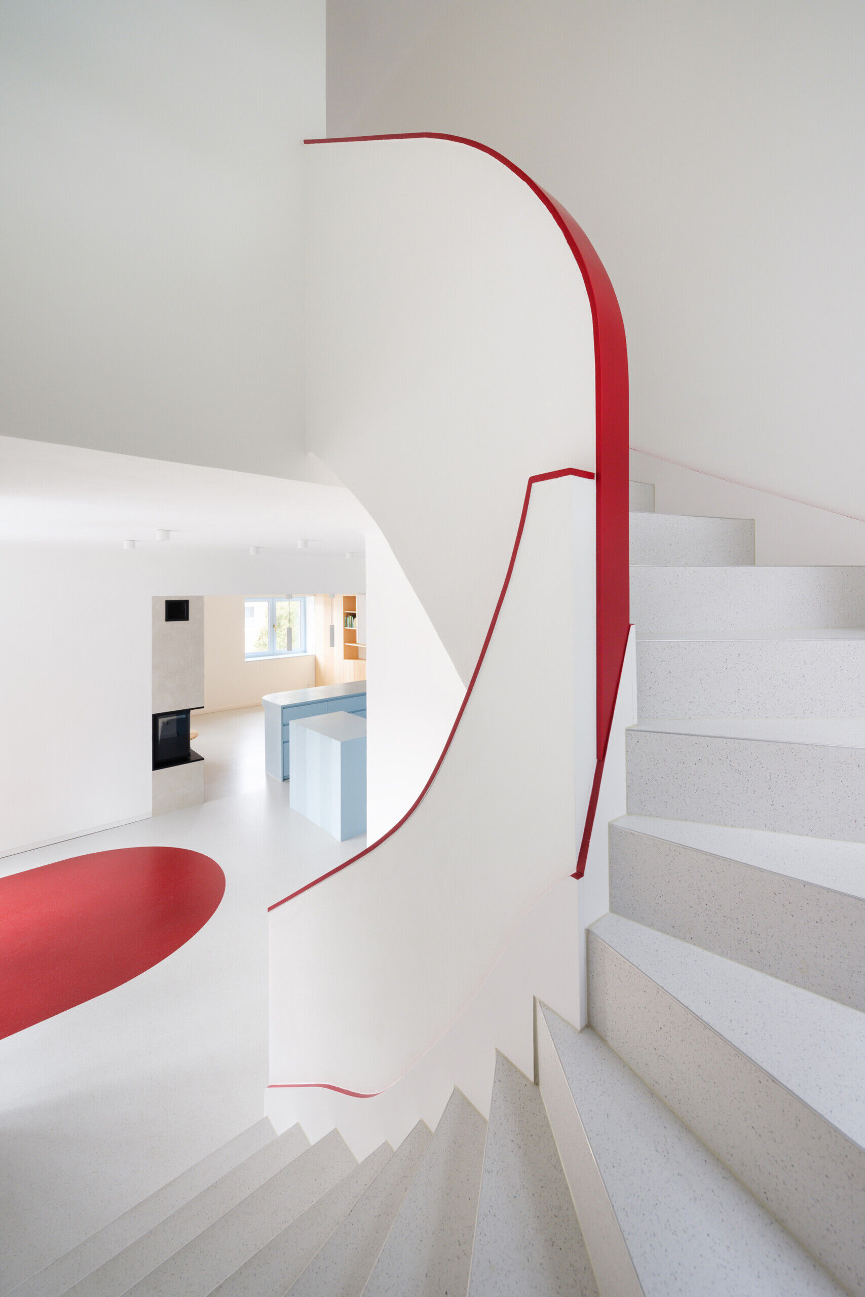 Discover the colorful architectural details inside this modernist house renovation in Prague. A curved staircase with pale blue steps, slender red railings, and subtle red accents along doors, baseboards, and furniture introduces an unexpected design element.