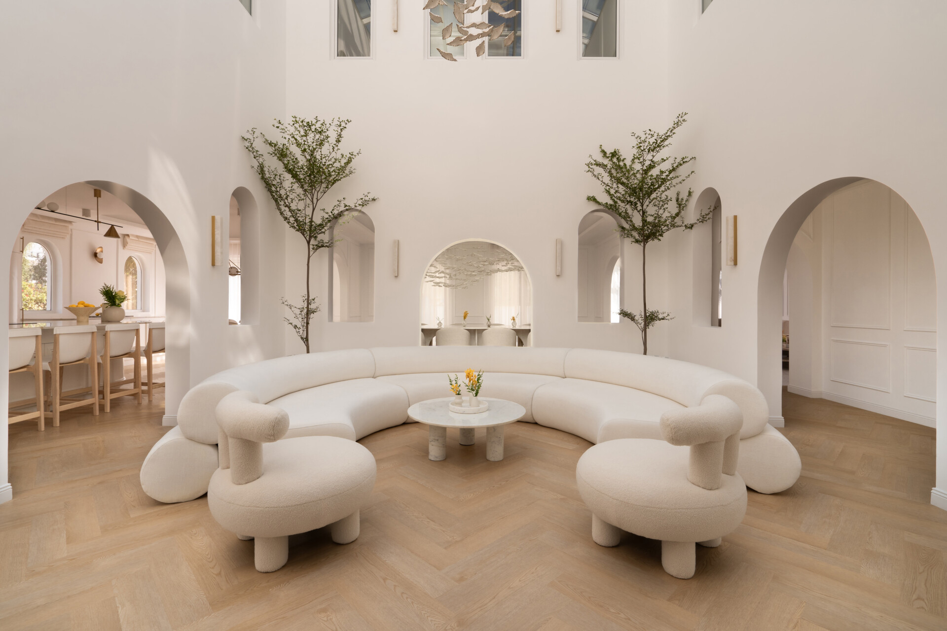 Discover the central courtyard inside The White Arcade, a Dubai villa renovated by D’Ora Tokai Designs. Featuring double-height ceilings, a glass roof, sculptural arches, a bespoke C-shaped sofa, indoor trees, and a floating leaf installation, this unique living space is filled with natural light.