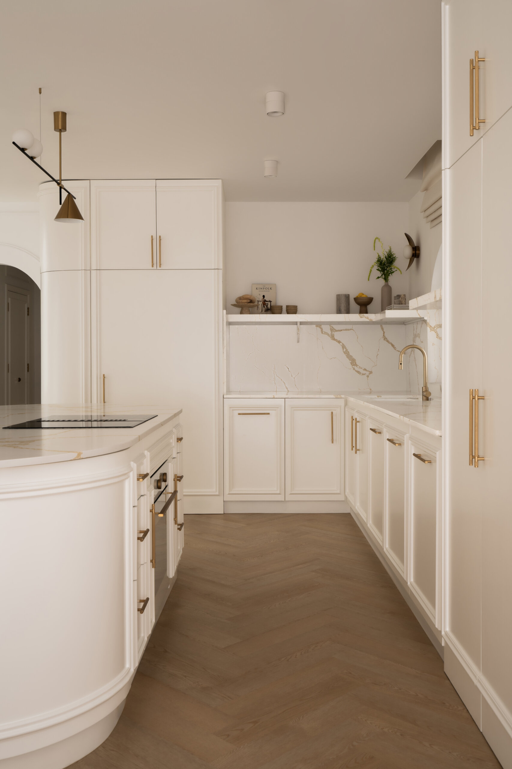 Explore this luxurious white kitchen by D’Ora Tokai Designs in Dubai. Featuring a large curved kitchen island, white stone countertops with gold veining, brass cabinet handles, arched windows, and contemporary pendant lighting, The White Arcade offers beautiful inspiration for an elegant modern kitchen.