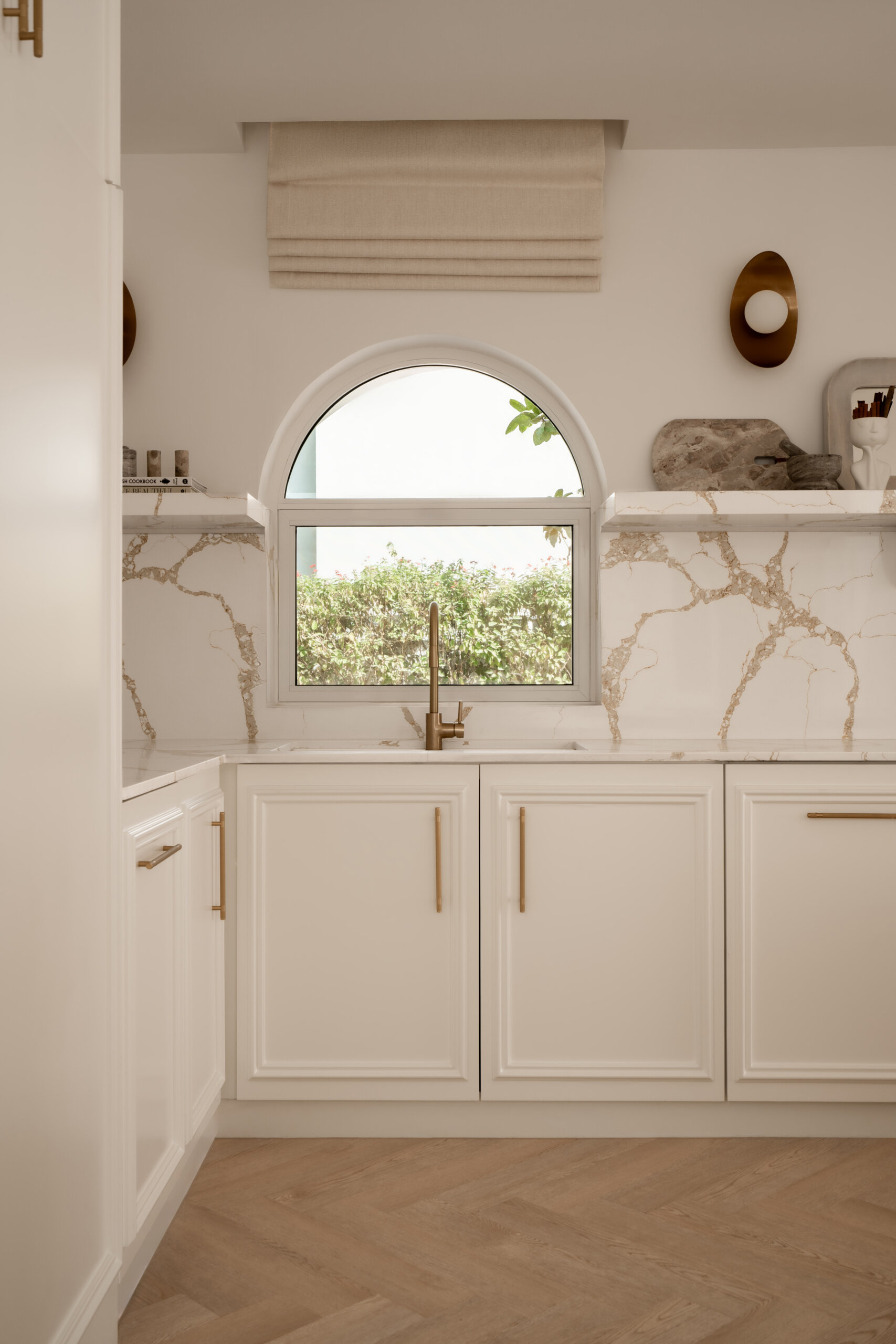 Explore this luxurious white kitchen by D’Ora Tokai Designs in Dubai. Featuring a large curved kitchen island, white stone countertops with gold veining, brass cabinet handles, arched windows, and contemporary pendant lighting, The White Arcade offers beautiful inspiration for an elegant modern kitchen.
