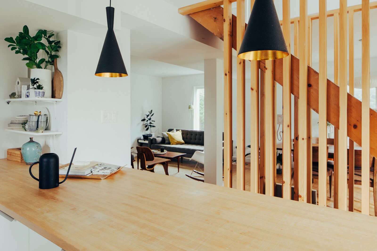 This small contemporary kitchen features pale wood cabinets, a large wooden breakfast bar, black pendant lights, hexagonal backsplash tiles, and a timber slat partition.