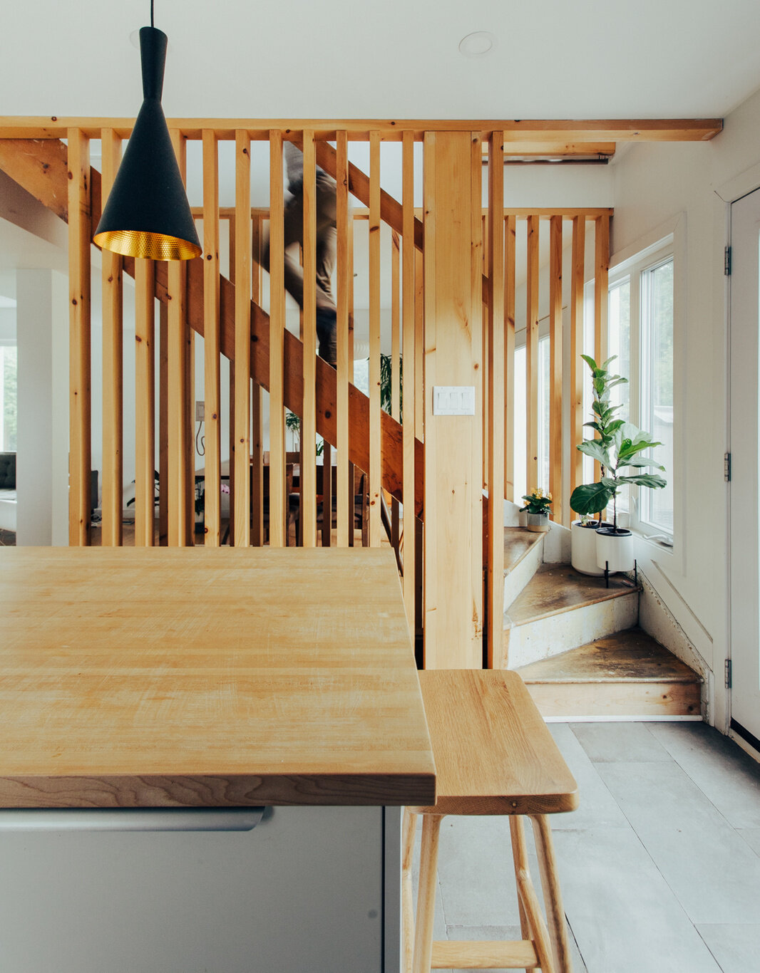 This small contemporary kitchen features pale wood cabinets, a large wooden breakfast bar, black pendant lights, hexagonal backsplash tiles, and a timber slat partition.