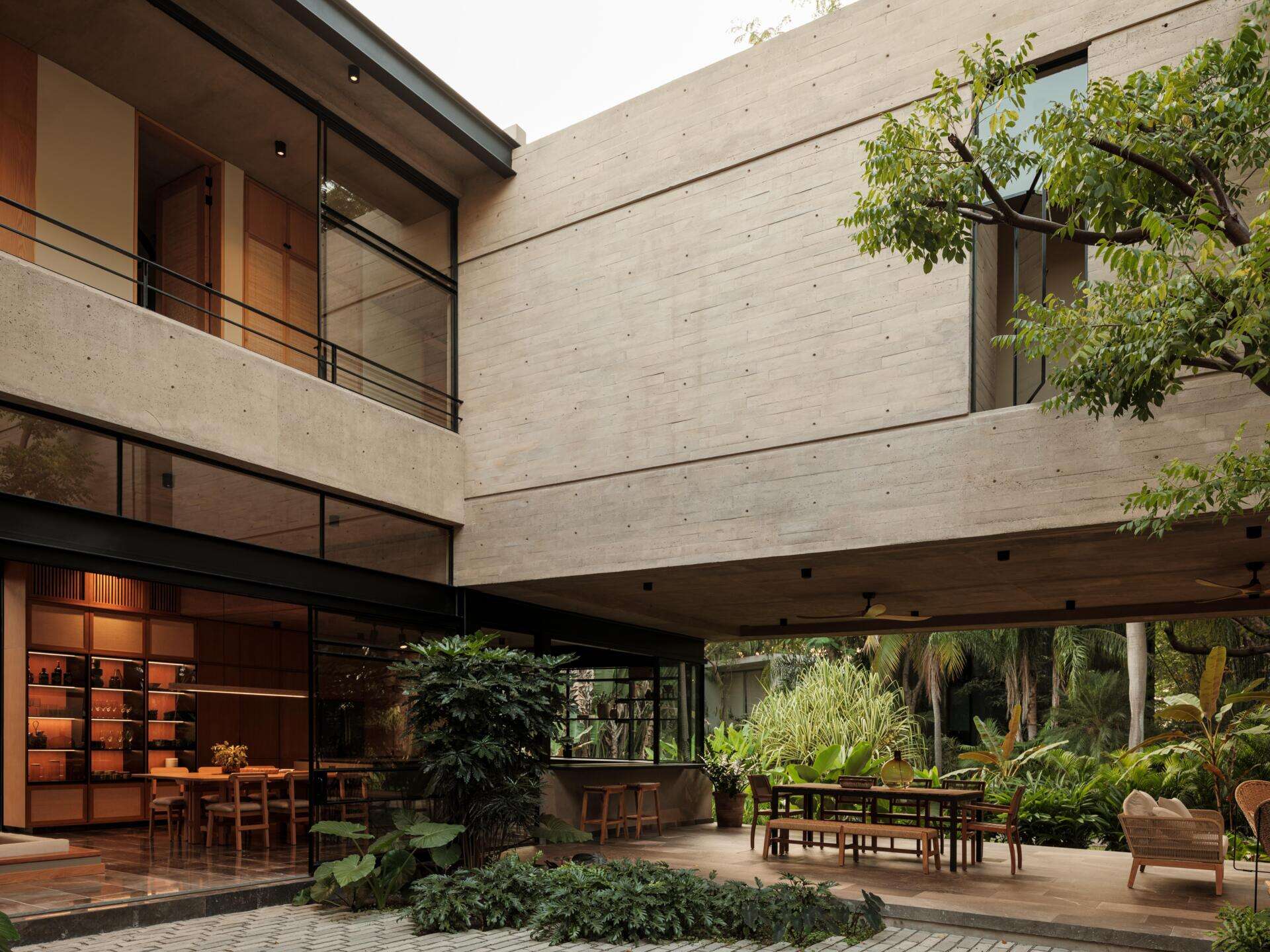 Discover a modern covered courtyard with outdoor dining, woven lounge furniture, concrete architecture, ceiling fans, and lush tropical landscaping. This Mexican home offers plenty of inspiration for indoor-outdoor living.