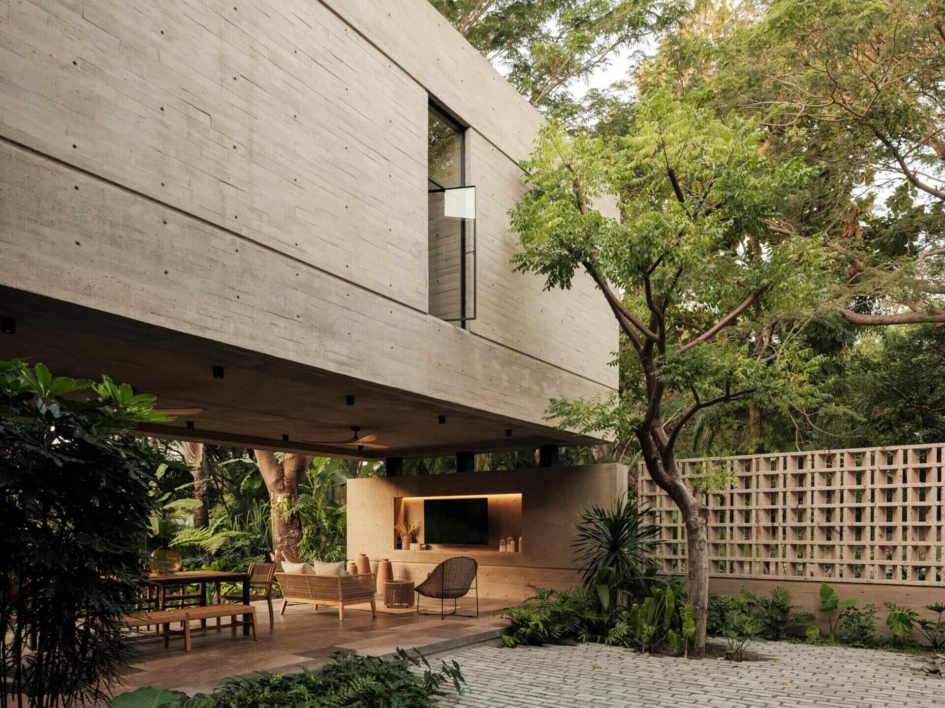 Discover a modern covered courtyard with outdoor dining, woven lounge furniture, concrete architecture, ceiling fans, and lush tropical landscaping. This Mexican home offers plenty of inspiration for indoor-outdoor living.