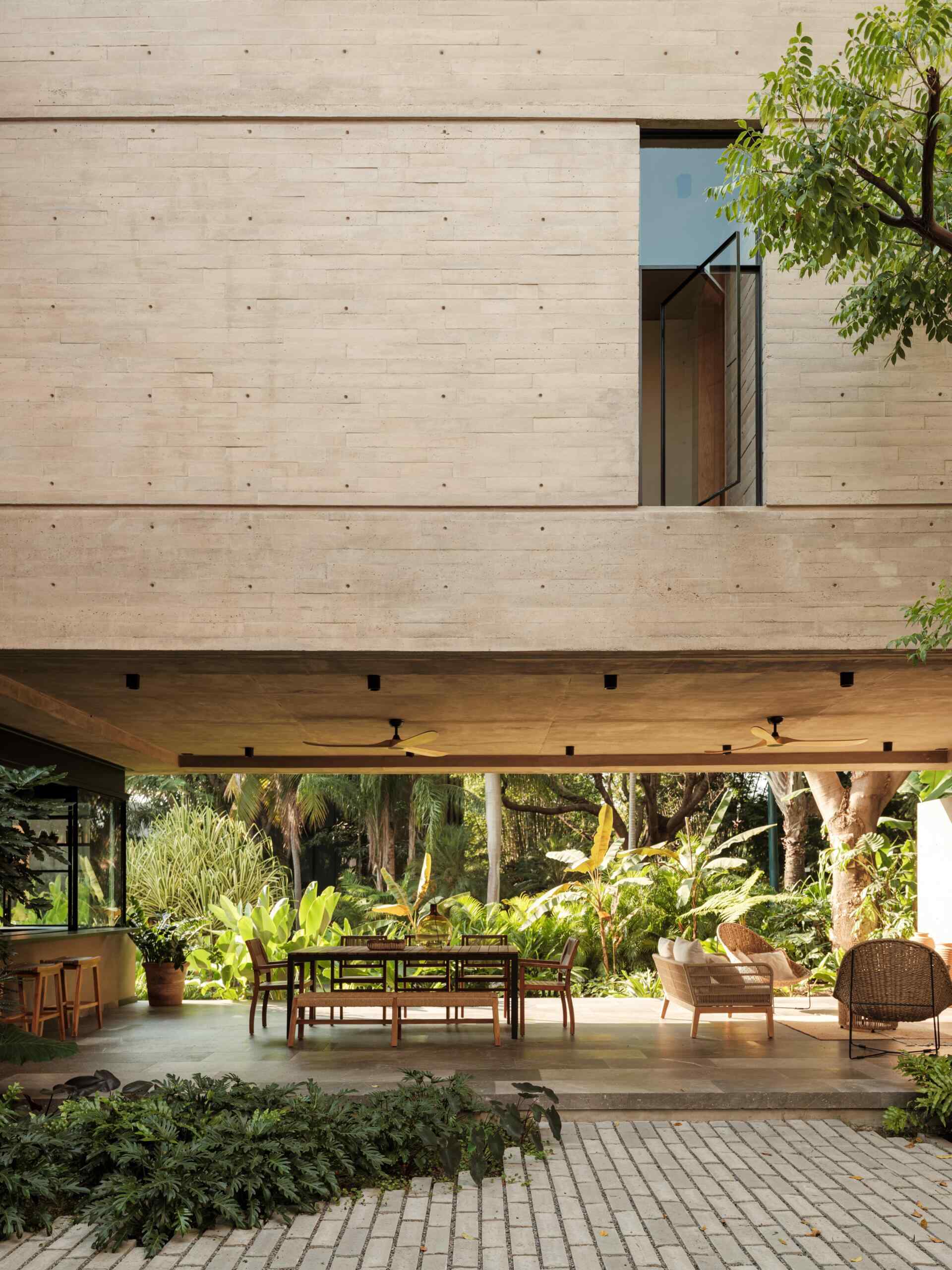 Discover a modern covered courtyard with outdoor dining, woven lounge furniture, concrete architecture, ceiling fans, and lush tropical landscaping. This Mexican home offers plenty of inspiration for indoor-outdoor living.