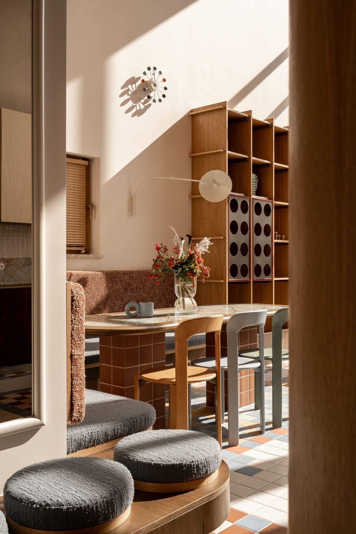 Get inspired by this contemporary dining area featuring a custom upholstered corner banquette, terracotta tiled base, stone dining table, and colorful mixed dining chairs.